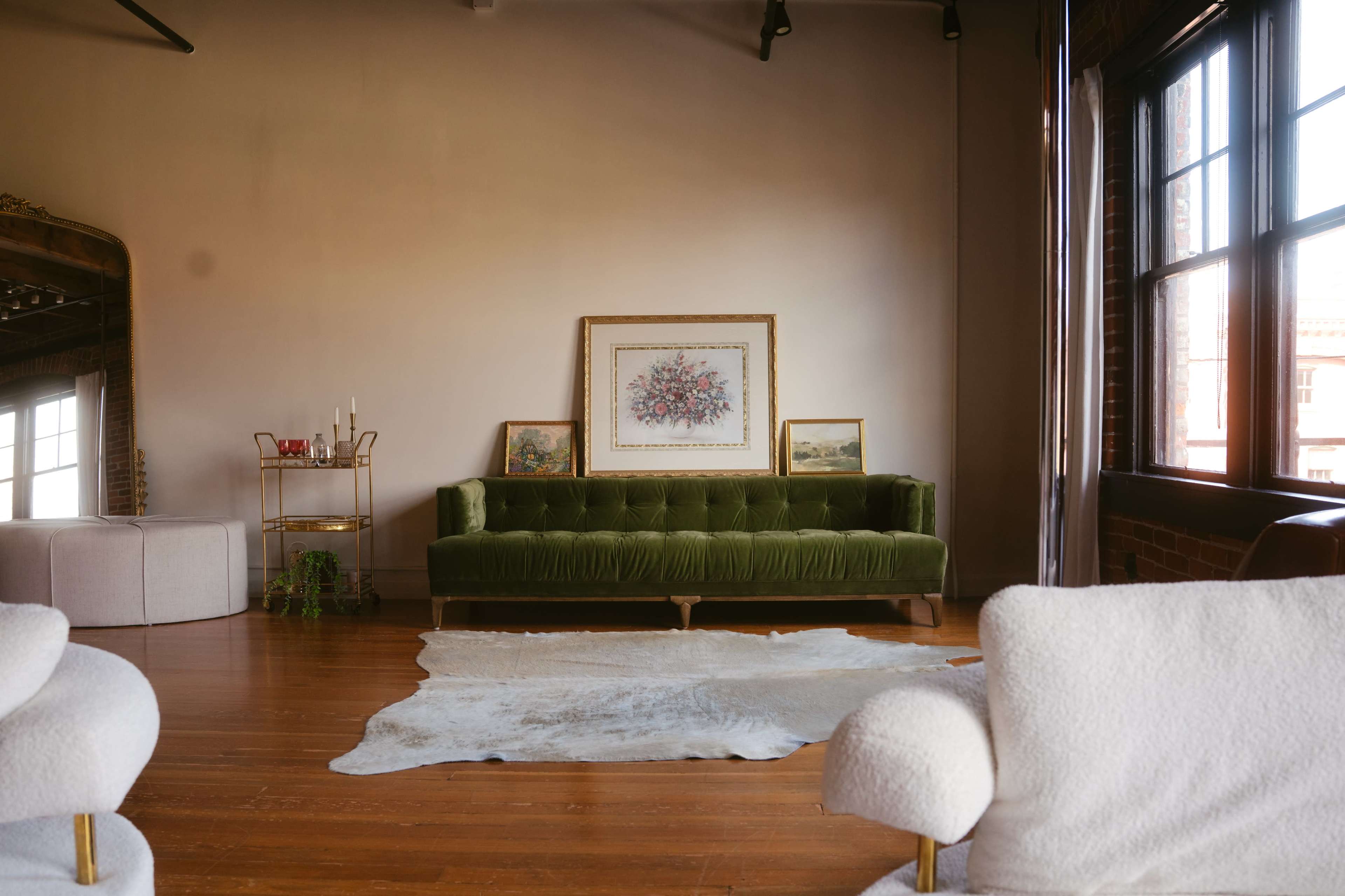 The image shows a spacious living area featuring a green velvet sofa, two white armchairs, and an artwork displayed above the sofa against a light-colored wall.