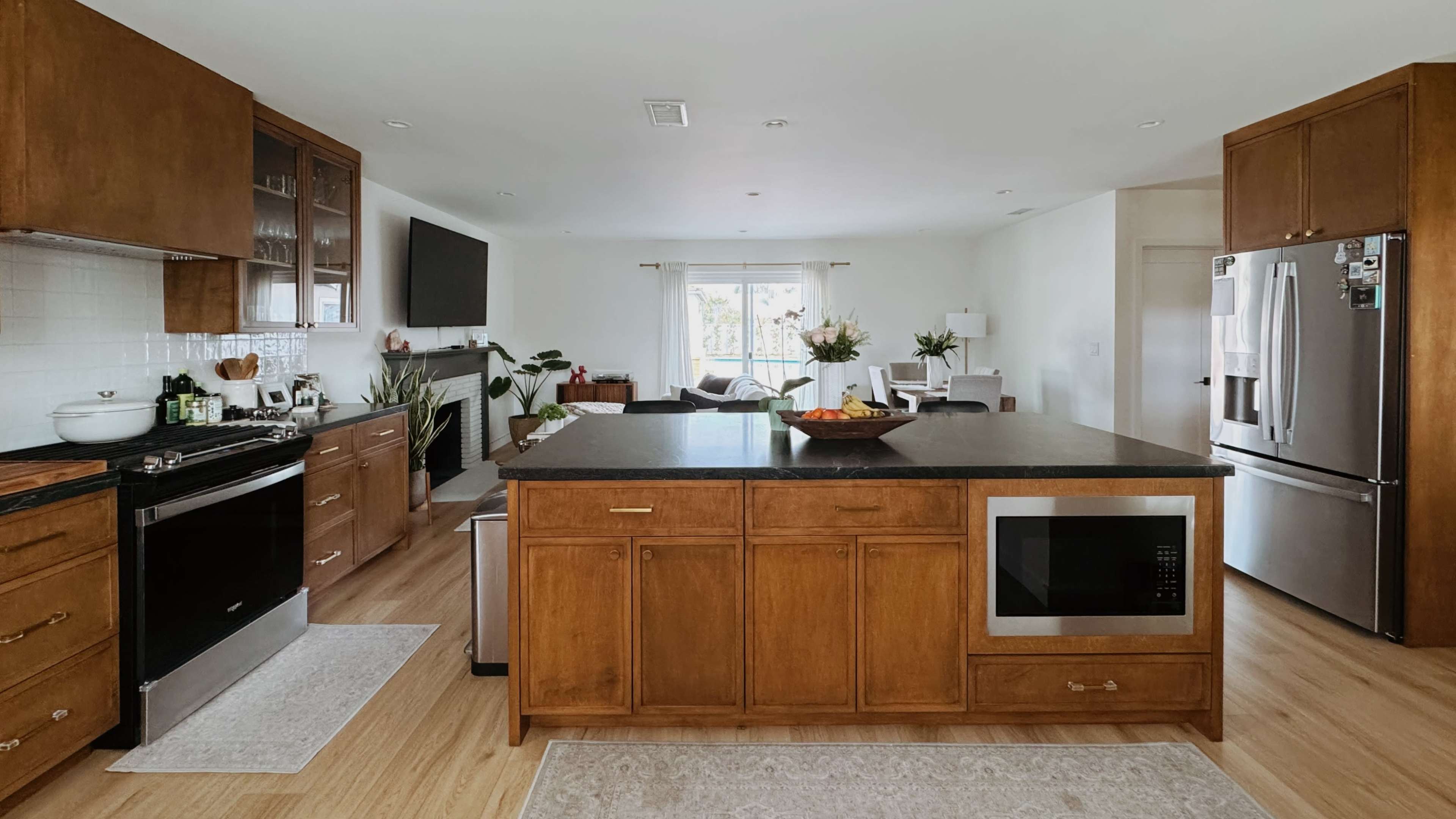 The kitchen features wood cabinetry, a large island with a microwave, and stainless steel appliances, creating an open and modern space.