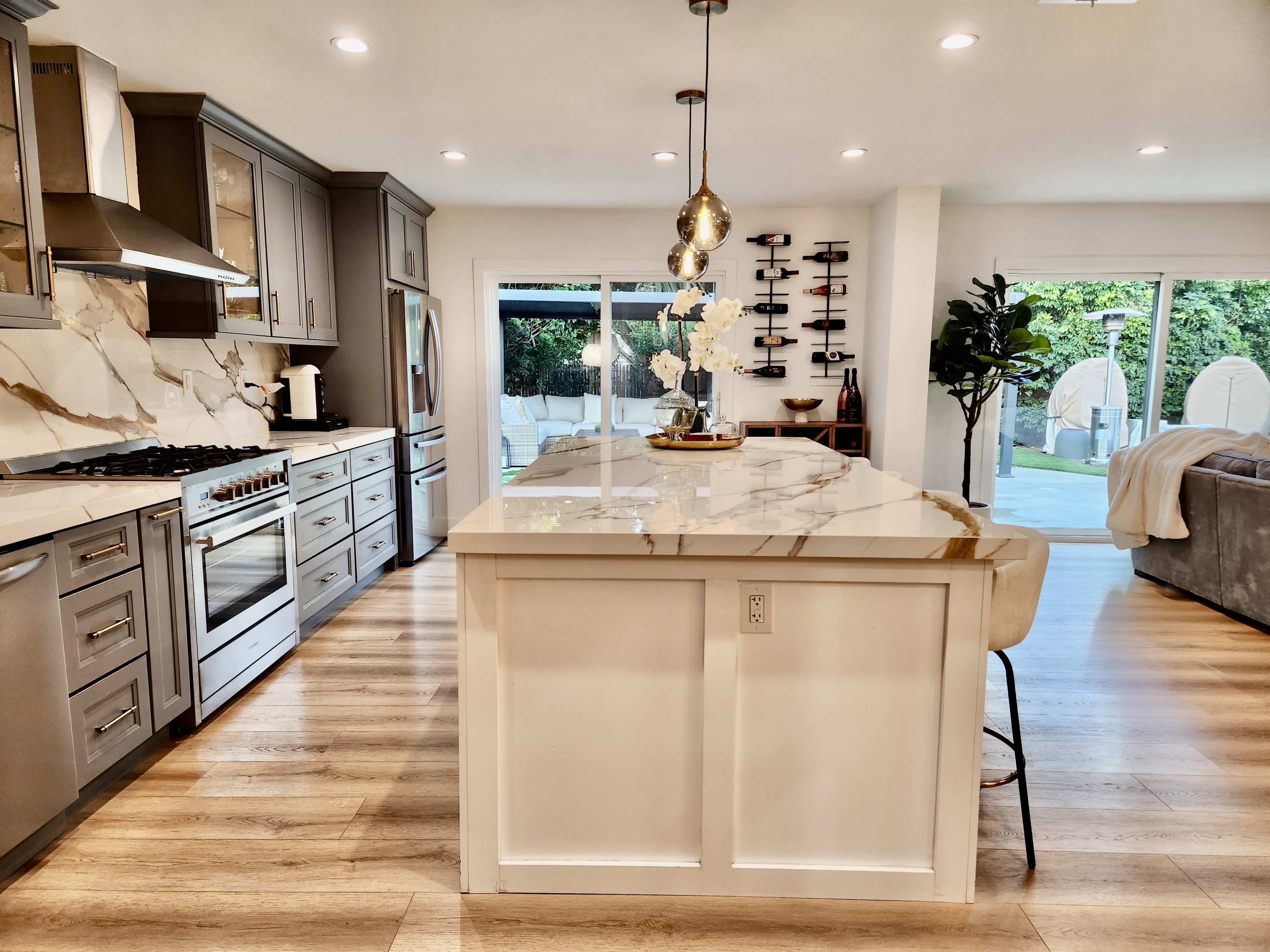 The kitchen features modern appliances, a central island with seating, and a view of an outdoor space through large sliding glass doors.