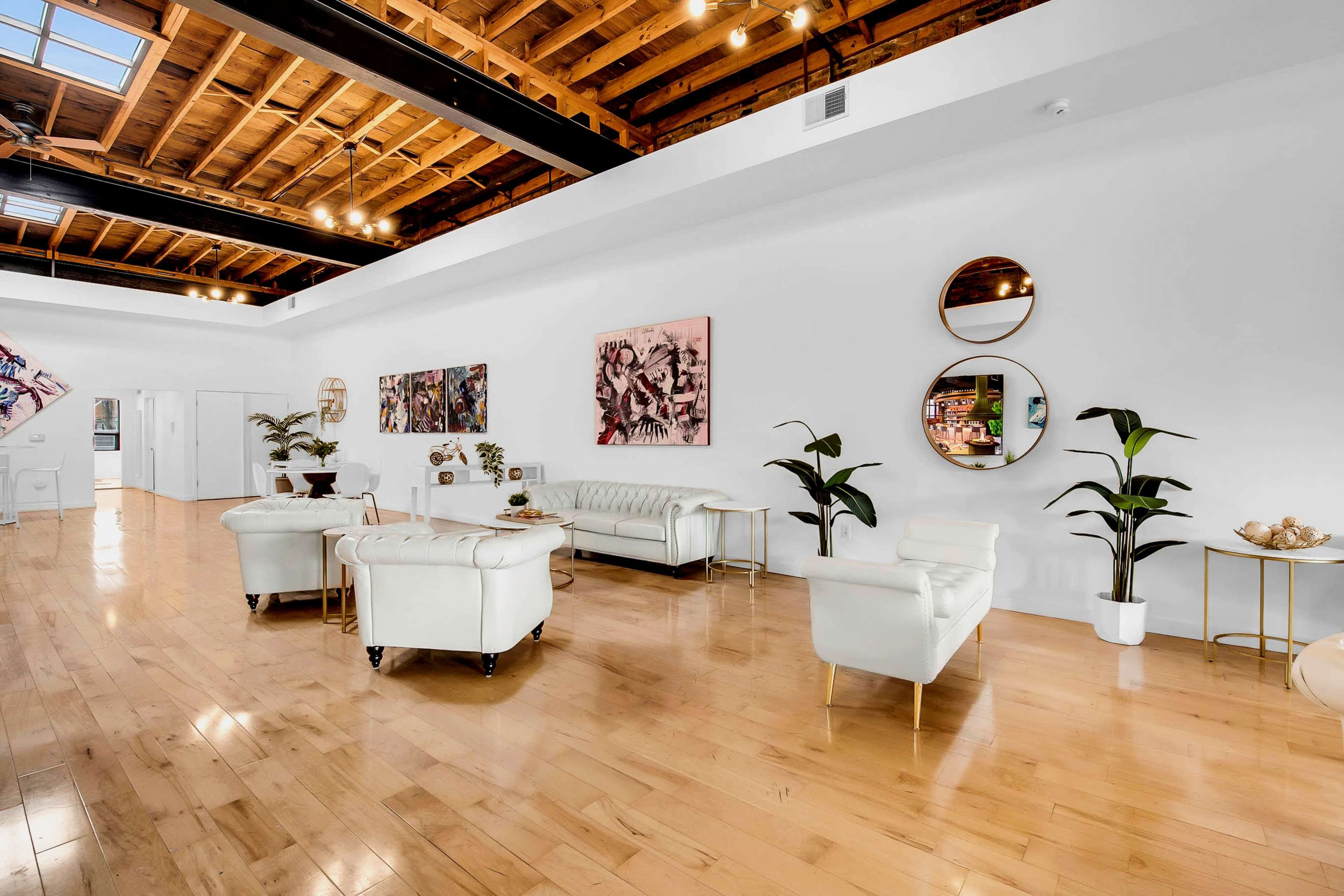 A bright, open interior space features white walls, wooden flooring, modern furnishings, and decorative art on display.