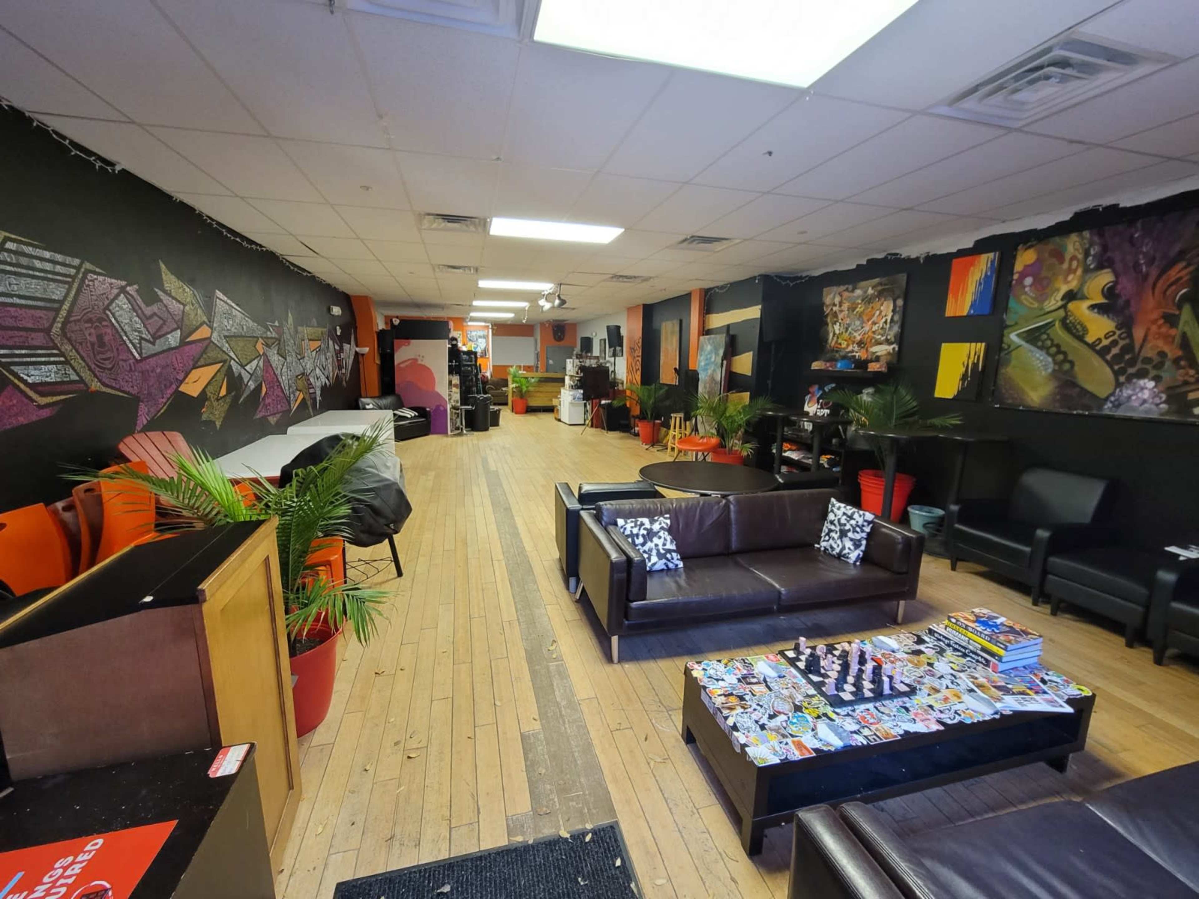 The interior of a lounge features dark walls adorned with colorful murals, a series of couches, and tables scattered throughout the open space.