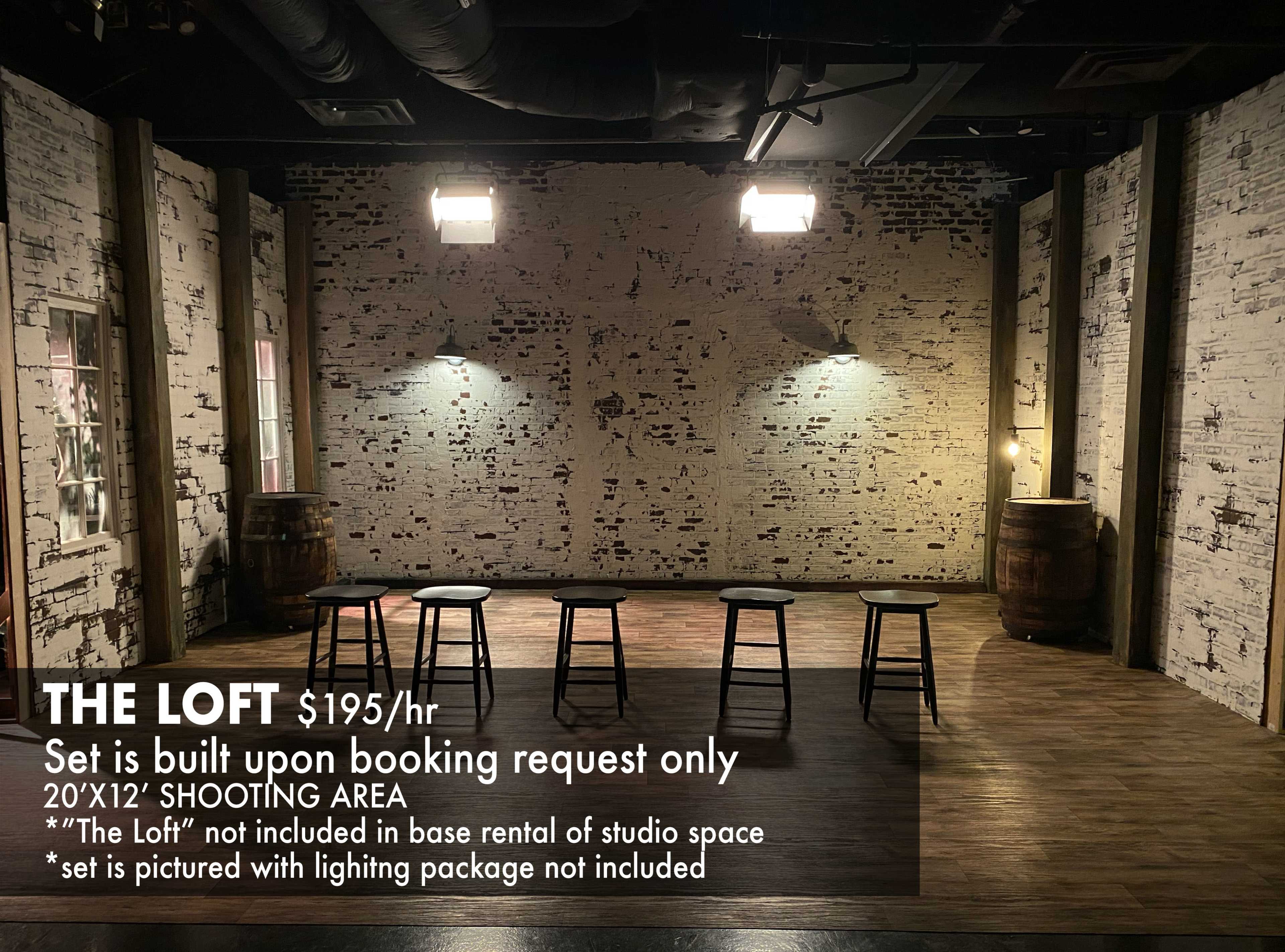 A spacious shooting area with a rustic backdrop features wooden flooring, exposed brick walls, and two barrels.