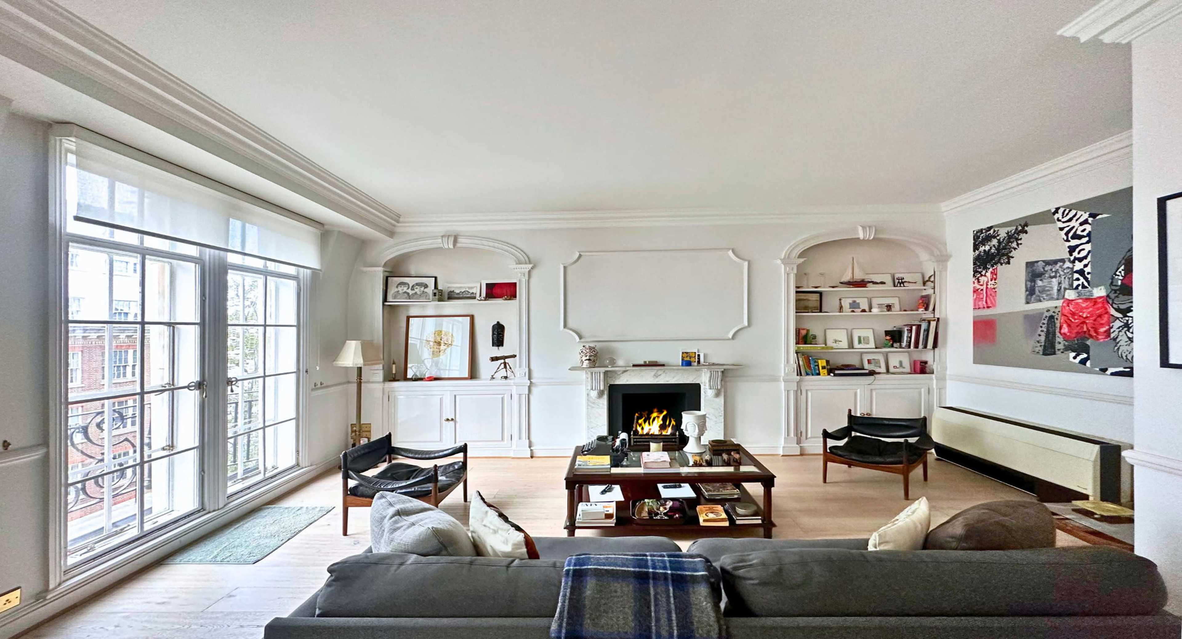 A modern living room featuring a fireplace, bookshelves, a coffee table, and large windows allowing natural light to enter.
