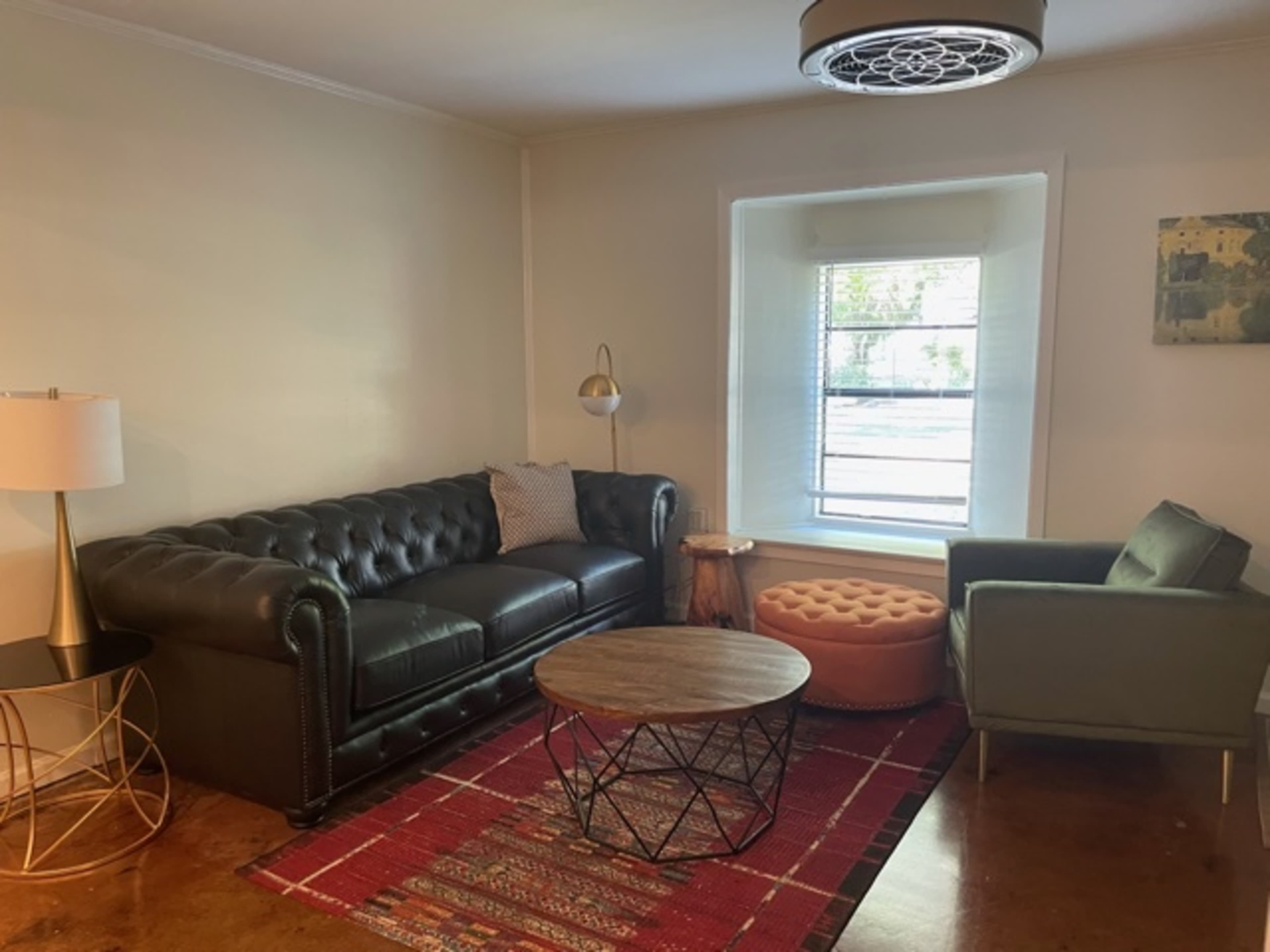 A living room with a black leather chesterfield sofa, a green armchair, a wooden coffee table, and a lamp beside a window.