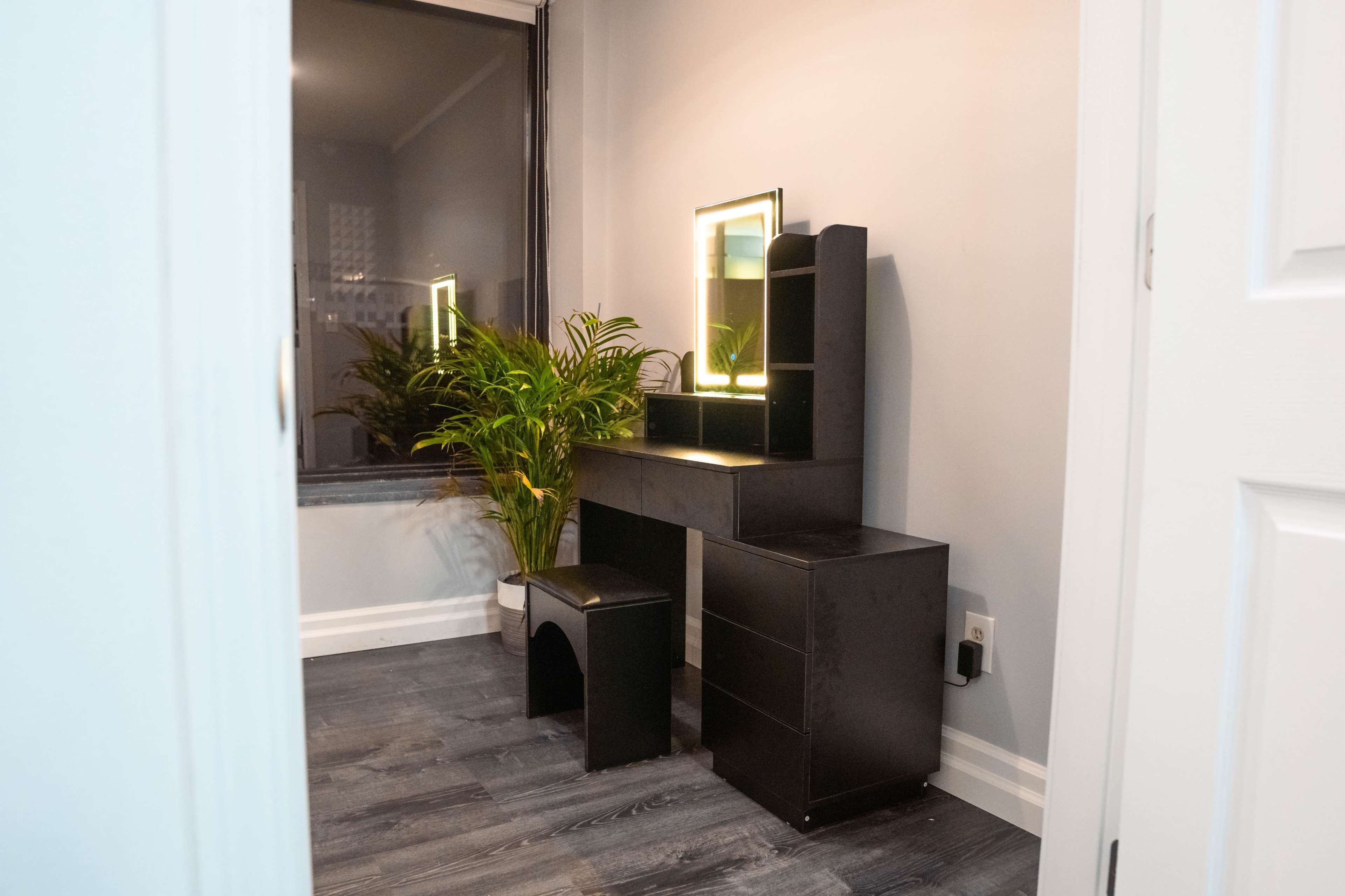 A minimalist black vanity set with a mirror and a small plant in a well-lit room with gray walls.