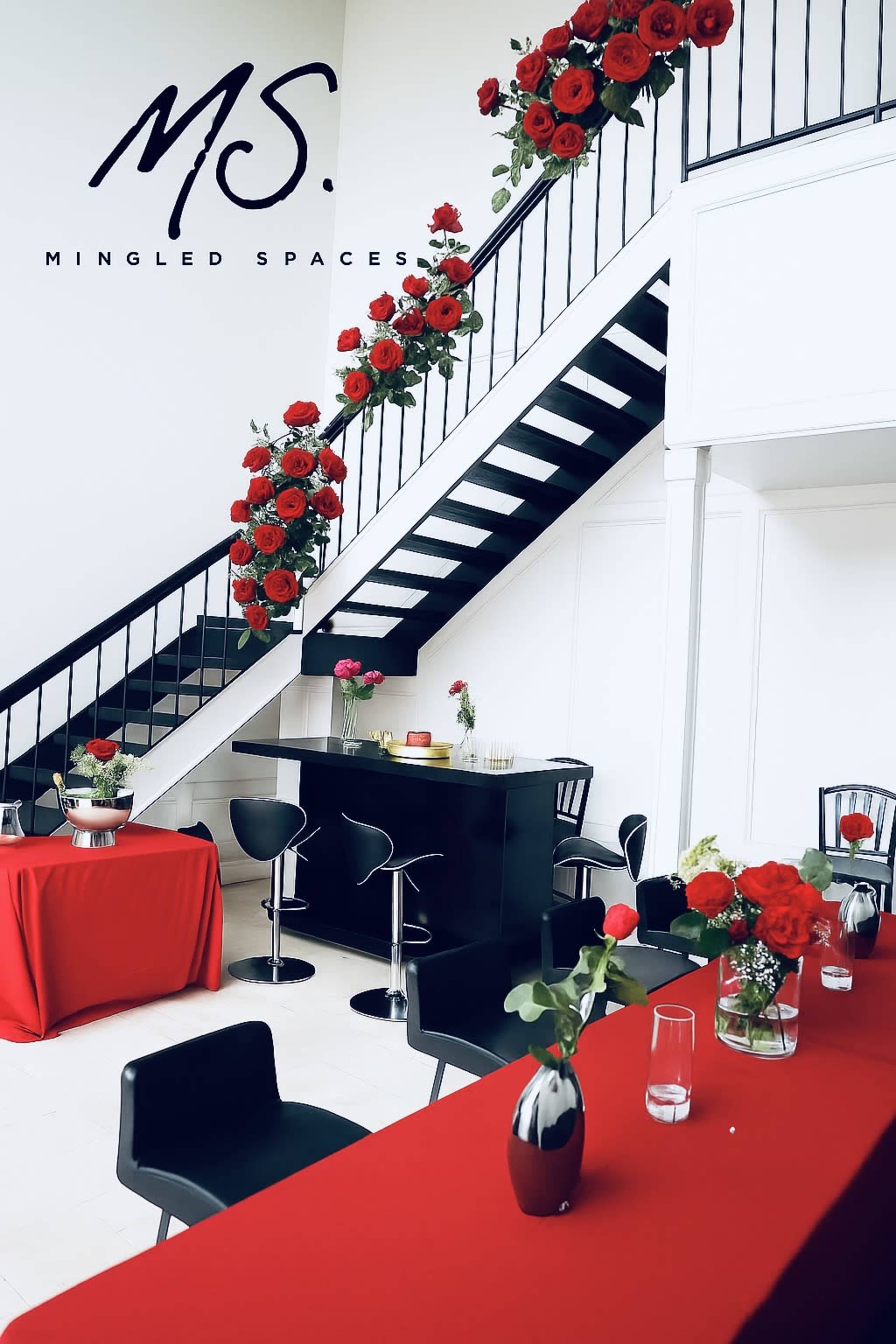 The image shows a modern indoor space featuring a staircase adorned with red roses and decorated tables with red tablecloths and floral arrangements.