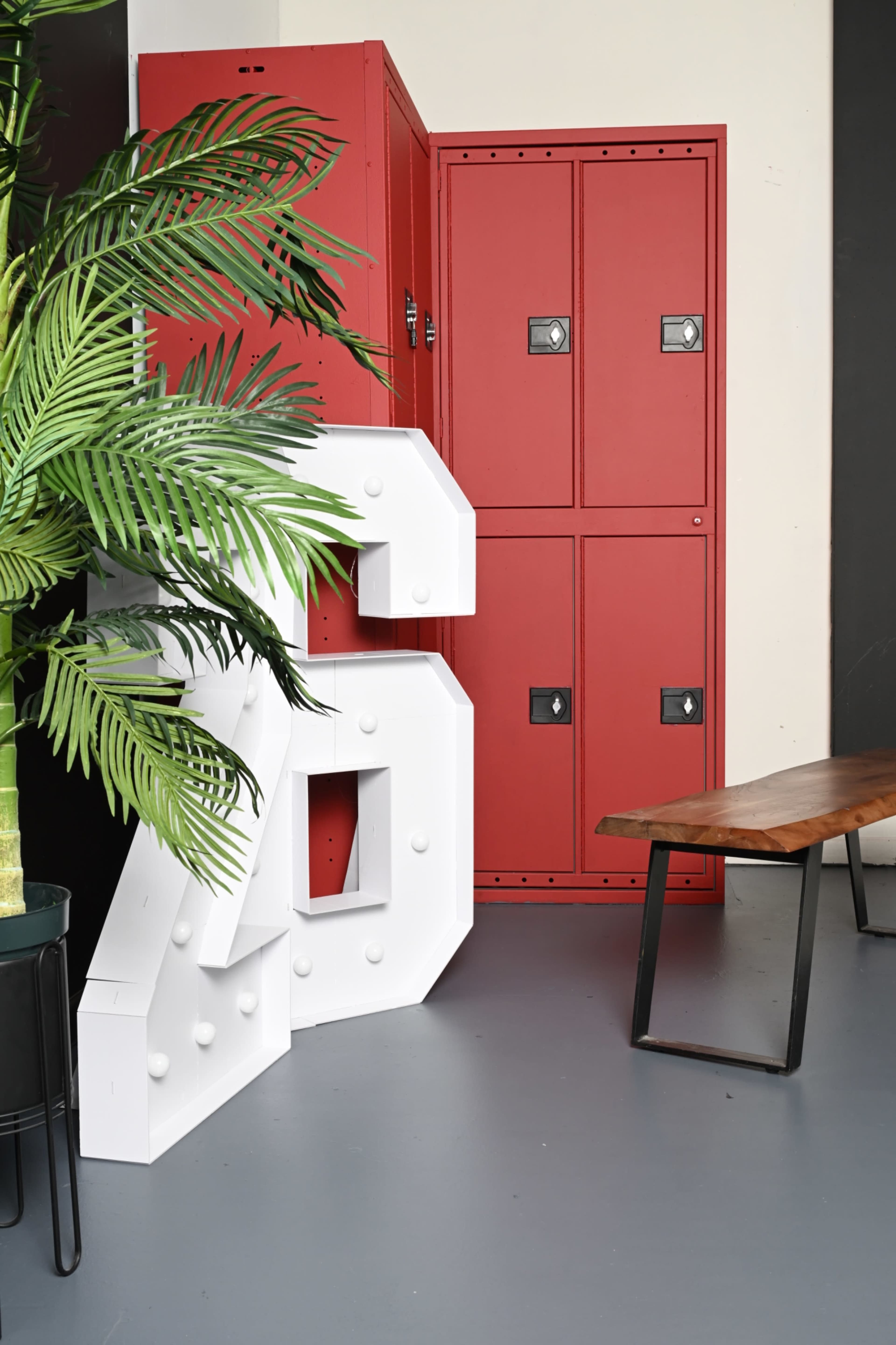 The image features a large white number "26" positioned beside red lockers and a wooden bench in a modern interior setting.