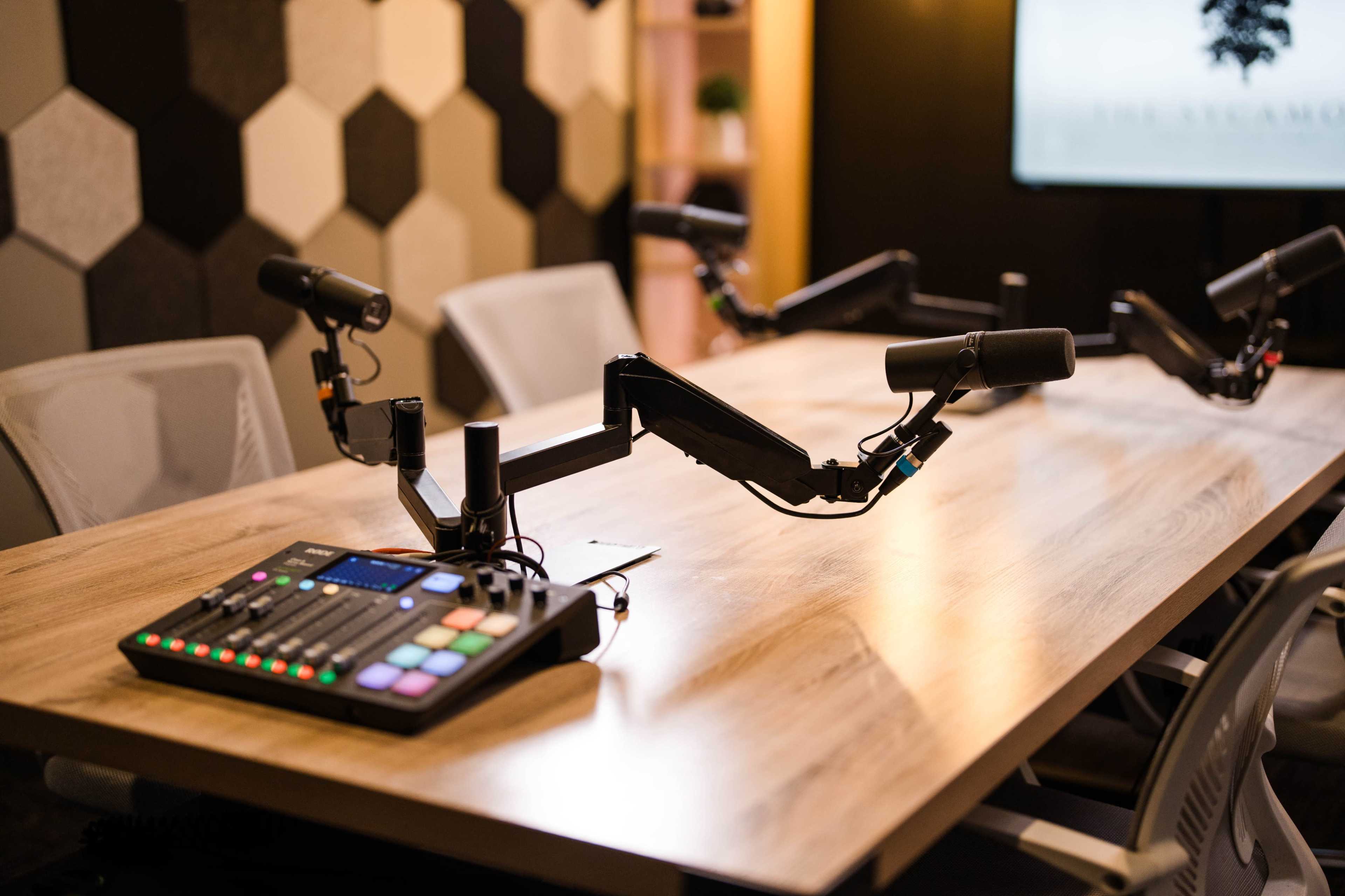 A conference table equipped with multiple microphone arms and a sound mixer, set in a modern, hexagon-patterned room.