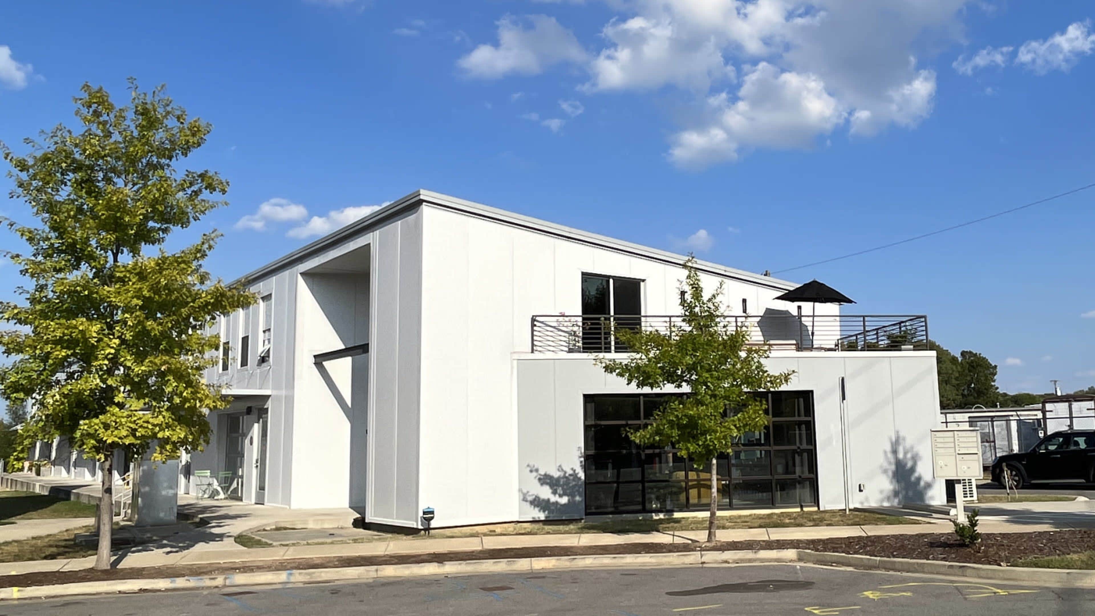 A white modern building with large windows and a rooftop terrace is set against a clear blue sky.
