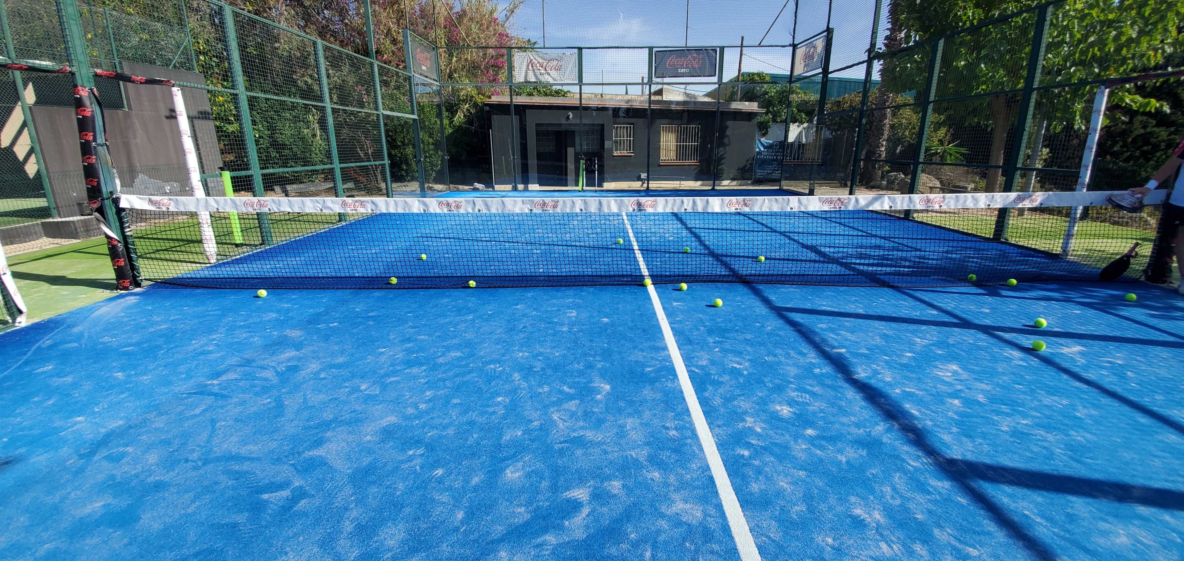 A blue tennis court with several green tennis balls scattered near the net.