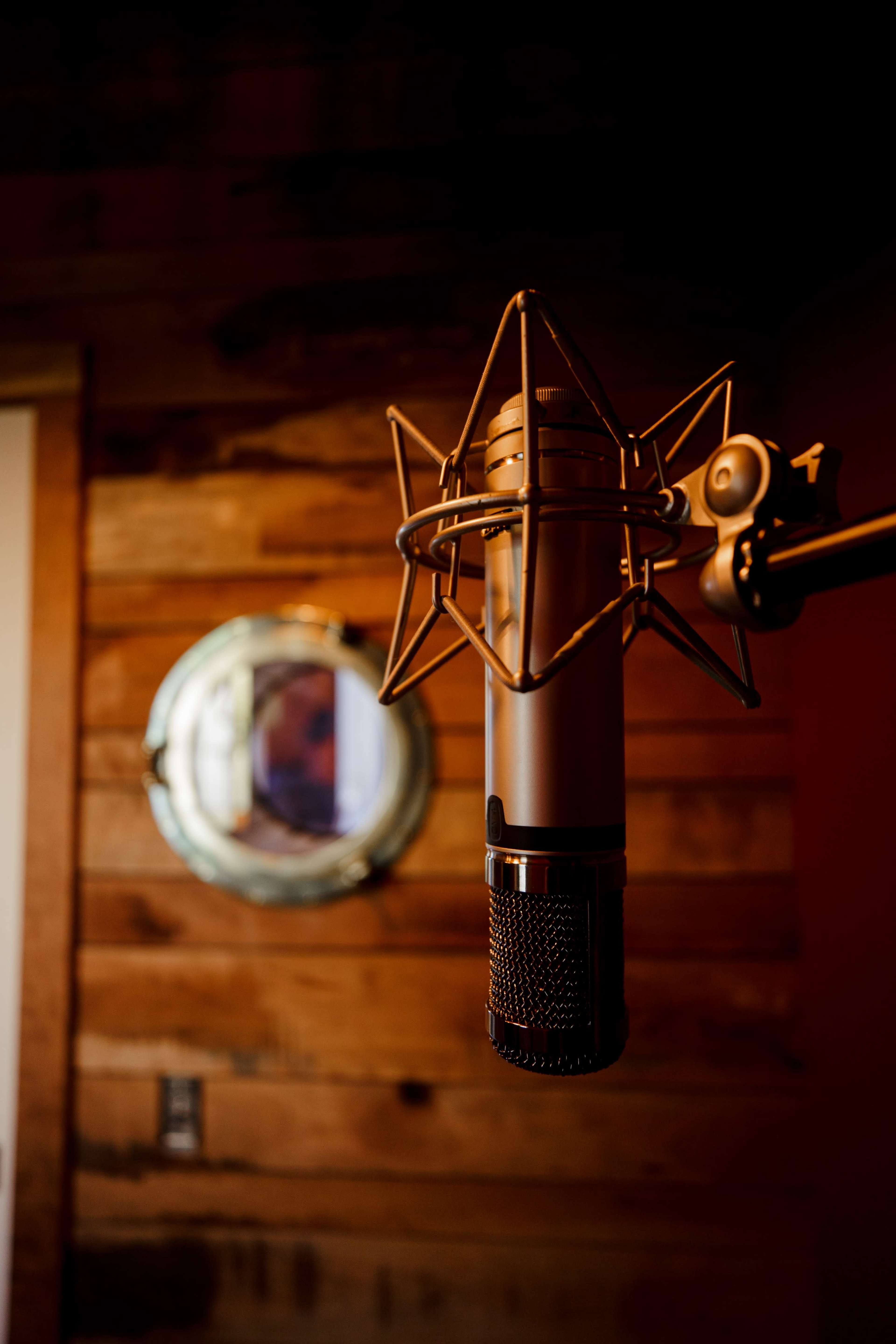 A close-up of a microphone mounted on a stand in a room with wooden walls and a round mirror in the background.