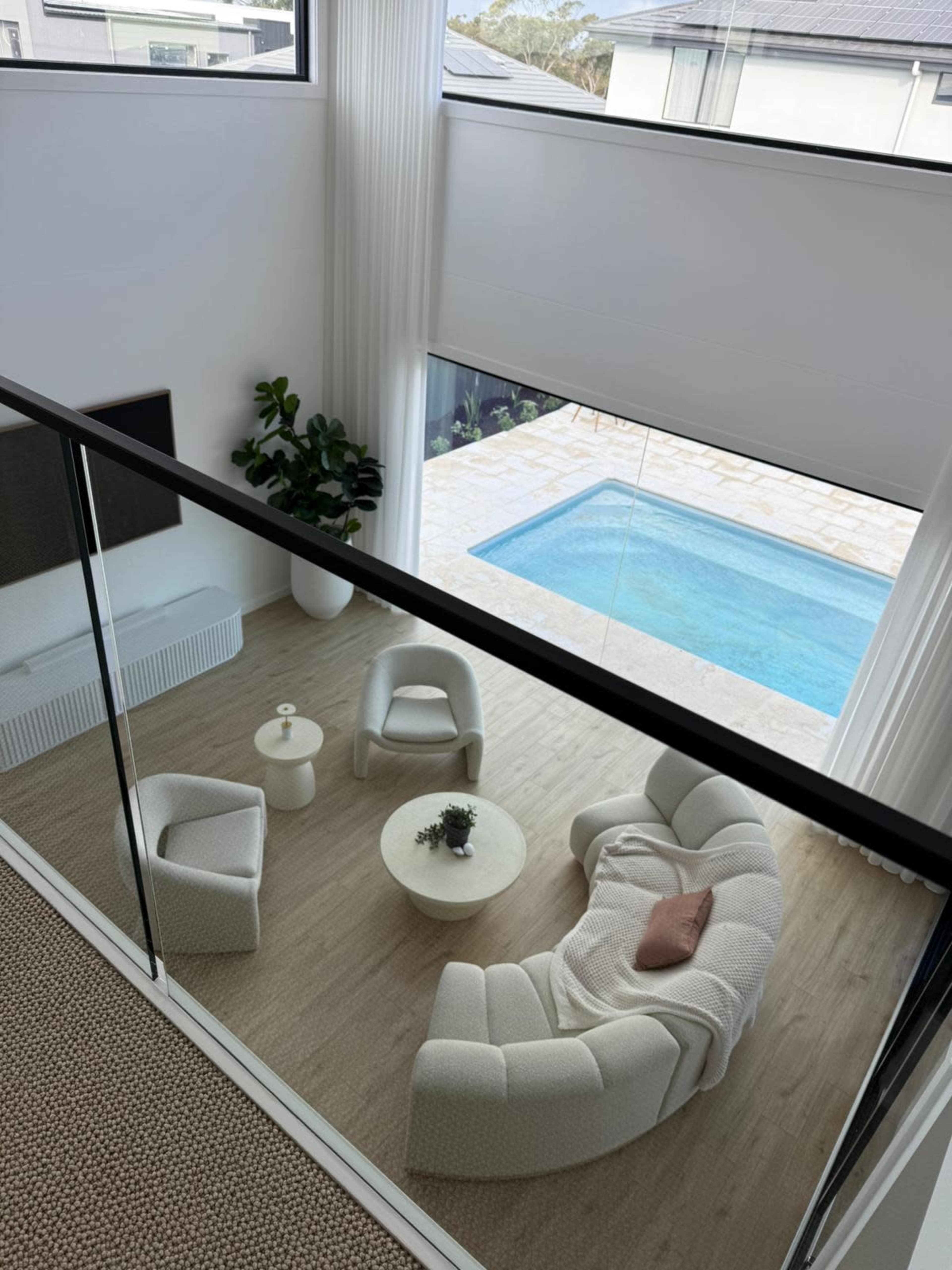 A modern interior features a light-filled living area with a curved sofa set, coffee table, and views of an outdoor pool.
