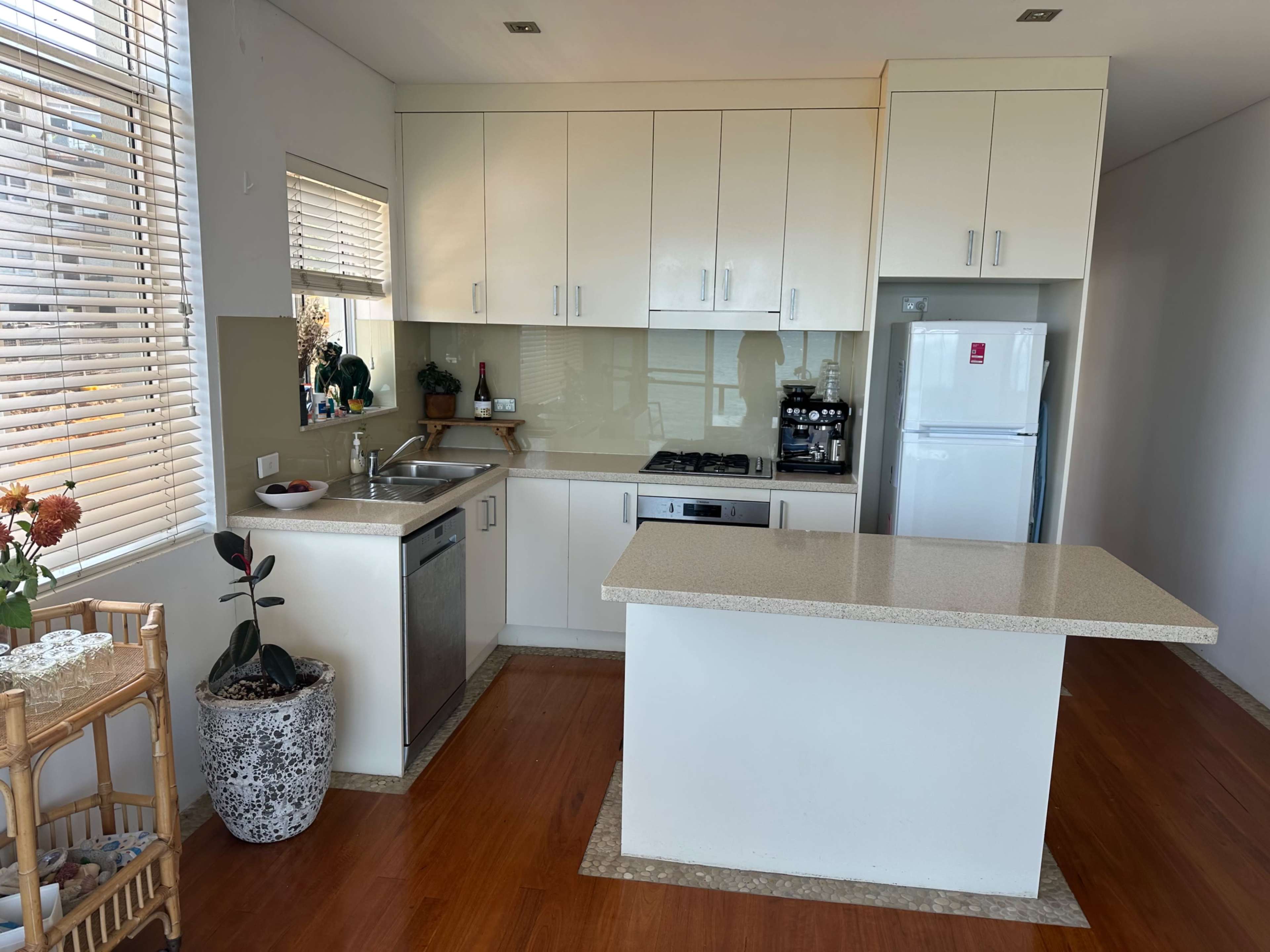 A modern kitchen with beige cabinets, a countertop island, stainless steel appliances, and natural light streaming through the window.