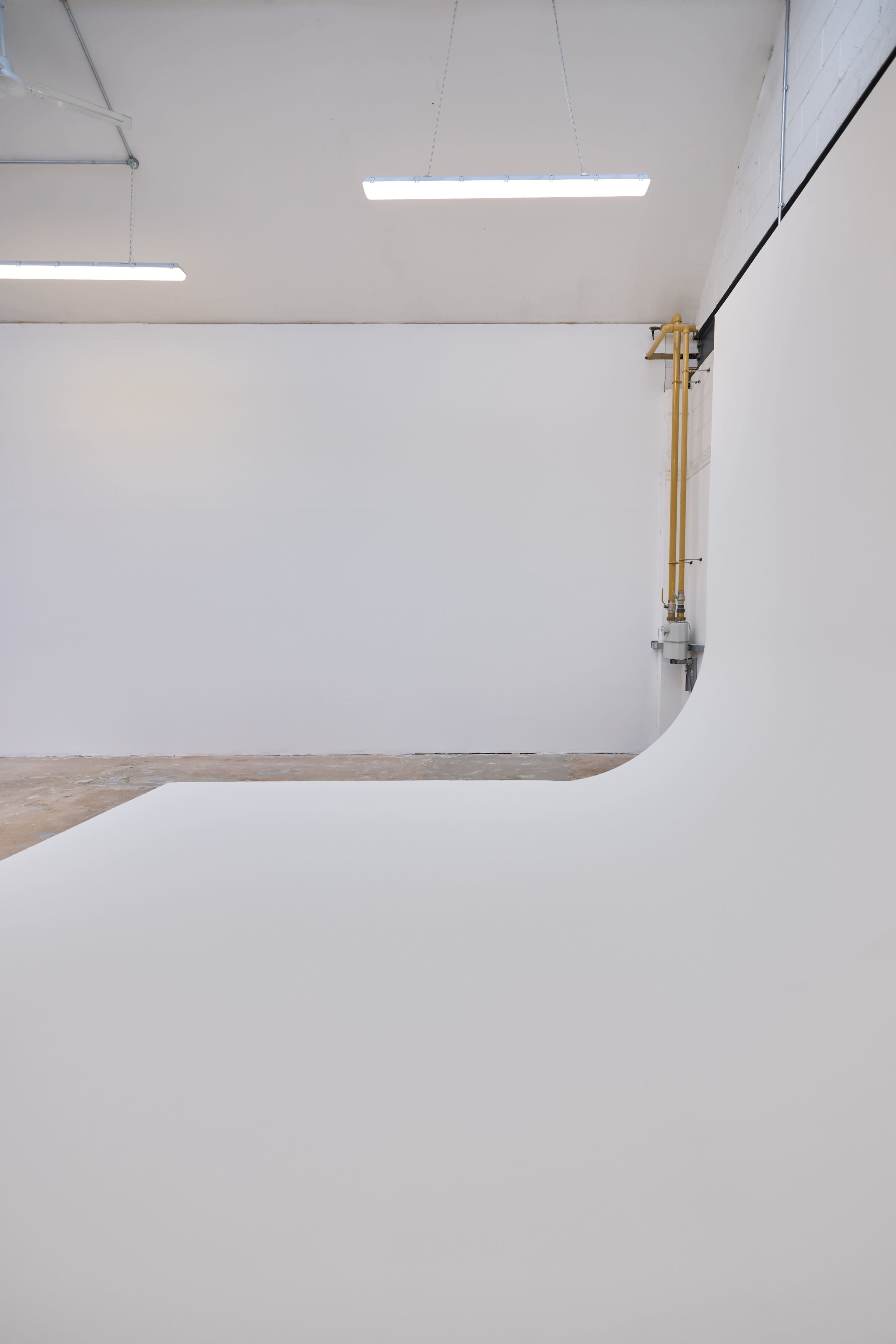 A brightly lit studio features a seamless white backdrop extending from the floor to the wall.