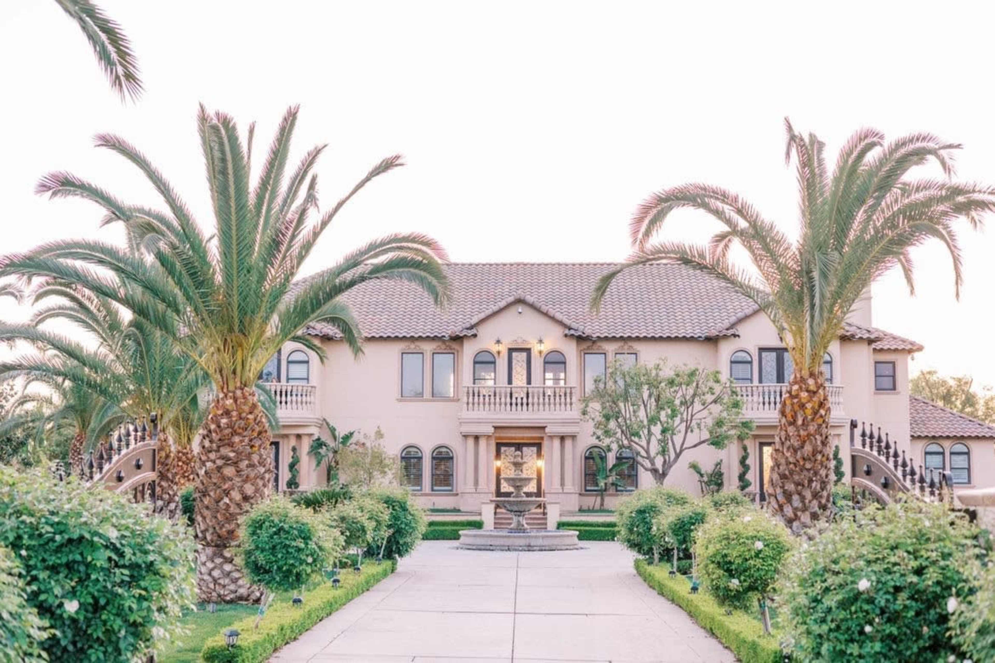 A large Mediterranean-style mansion framed by tall palm trees and neatly trimmed landscaping.