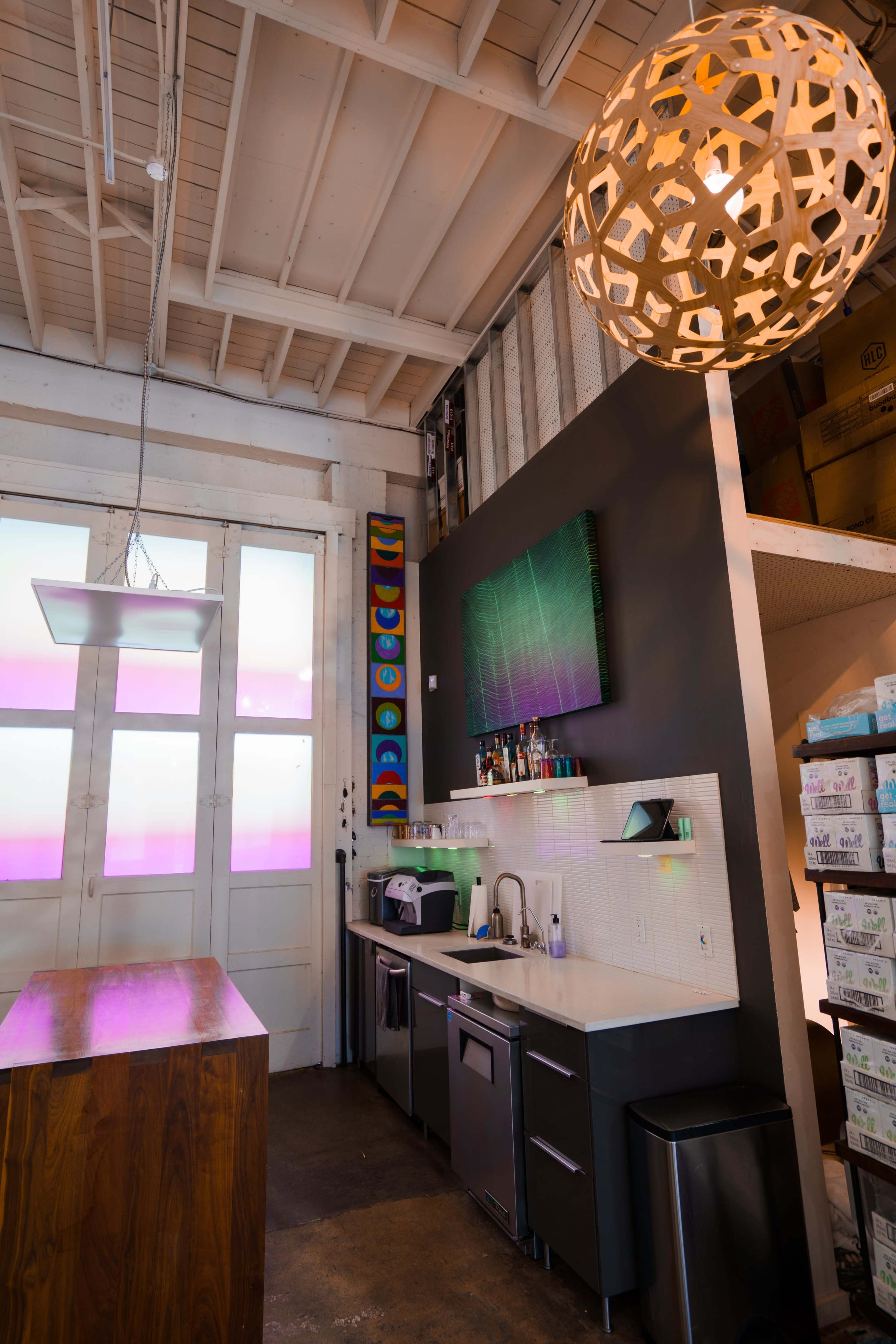 The image shows a modern kitchen area with a large pendant light, a counter with a sink, and colorful artwork hanging on the walls.