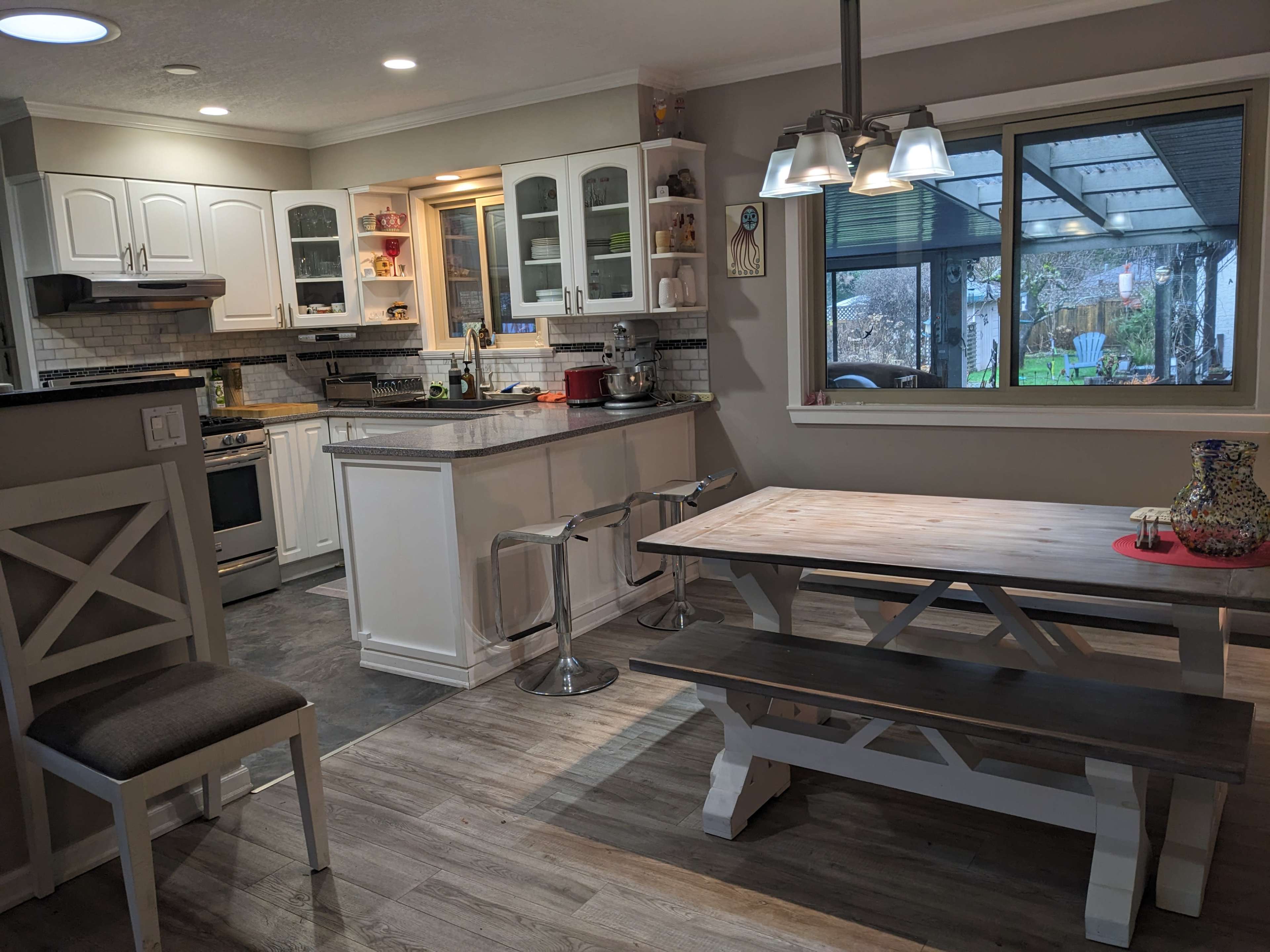The image shows a kitchen and dining area featuring white cabinetry, a wooden dining table, and a sliding glass door leading to an outdoor space.