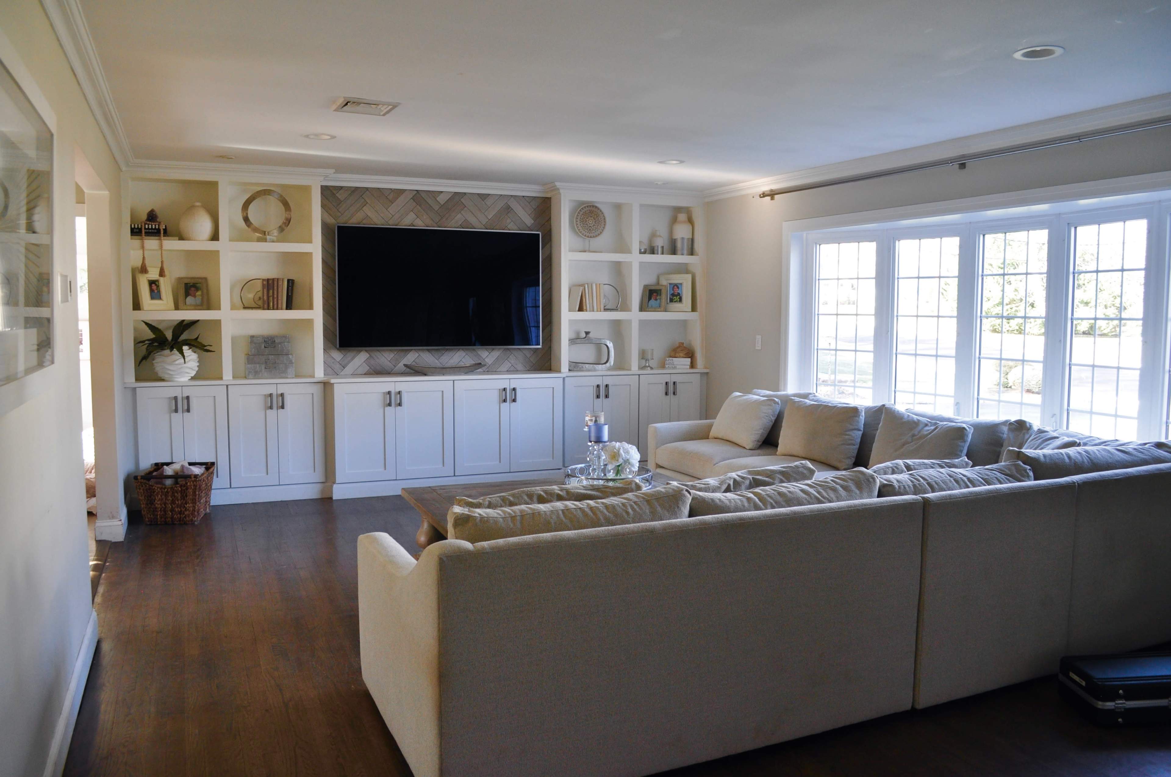The living room features a large sectional sofa facing a mounted television on a white cabinet, with built-in shelves displaying decorative items.