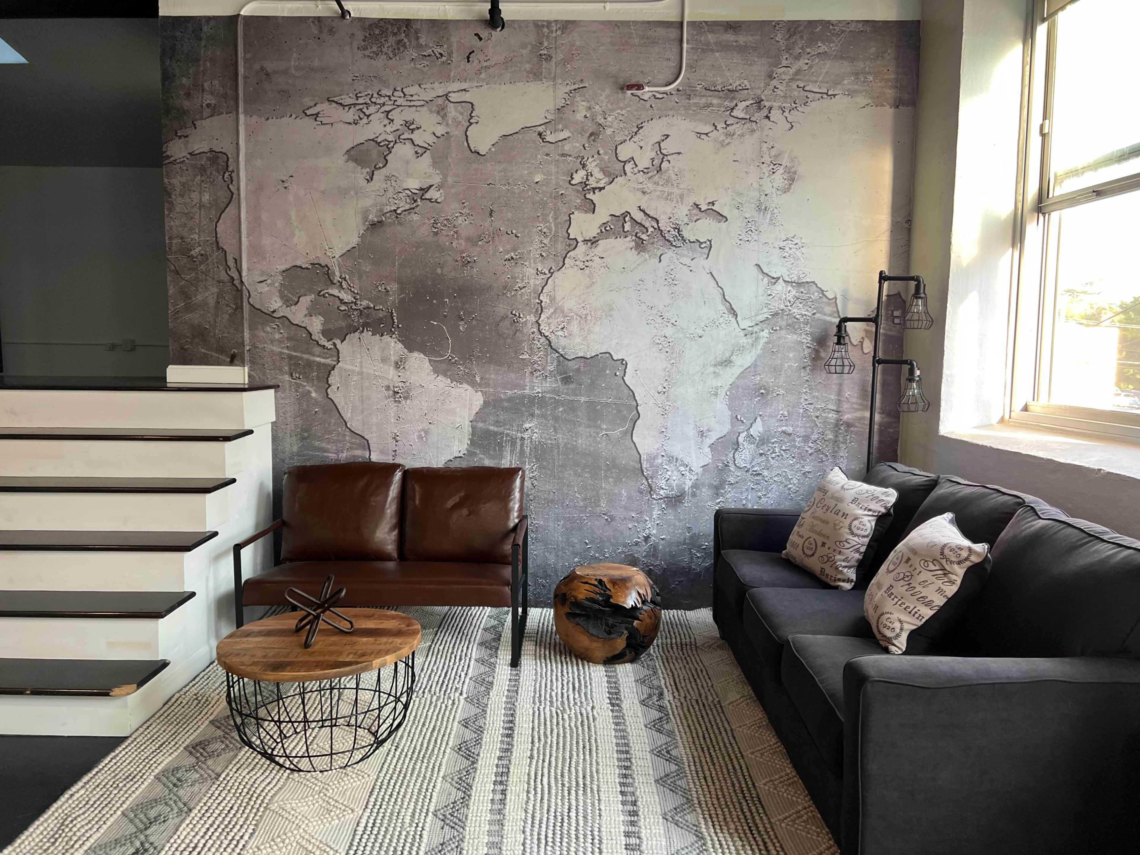 A cozy seating area featuring a brown leather loveseat and a dark sofa against a wall with a world map mural, accompanied by a wooden coffee table and patterned rug.