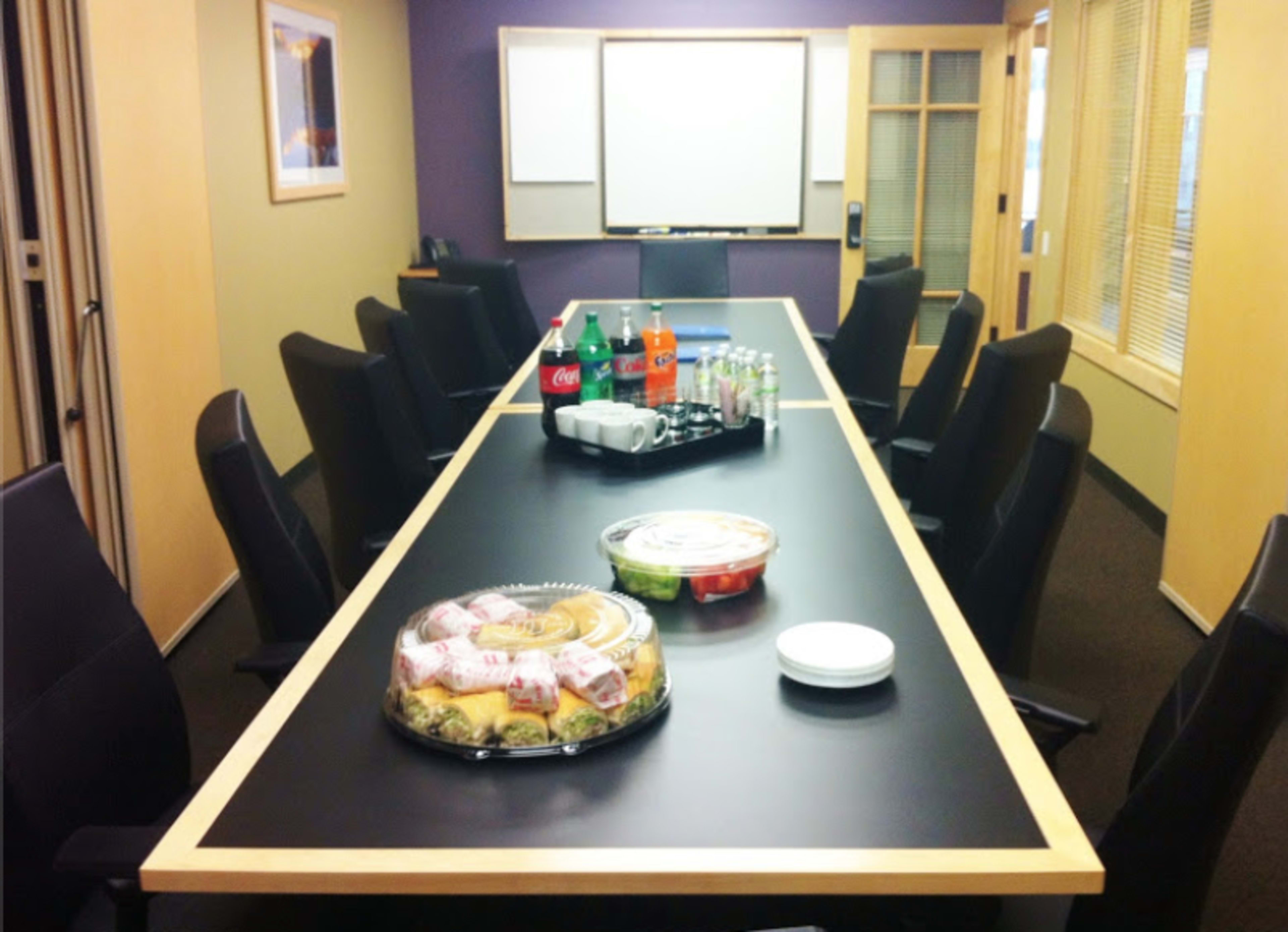 A conference room features a long table with plates of food and various beverages on display.