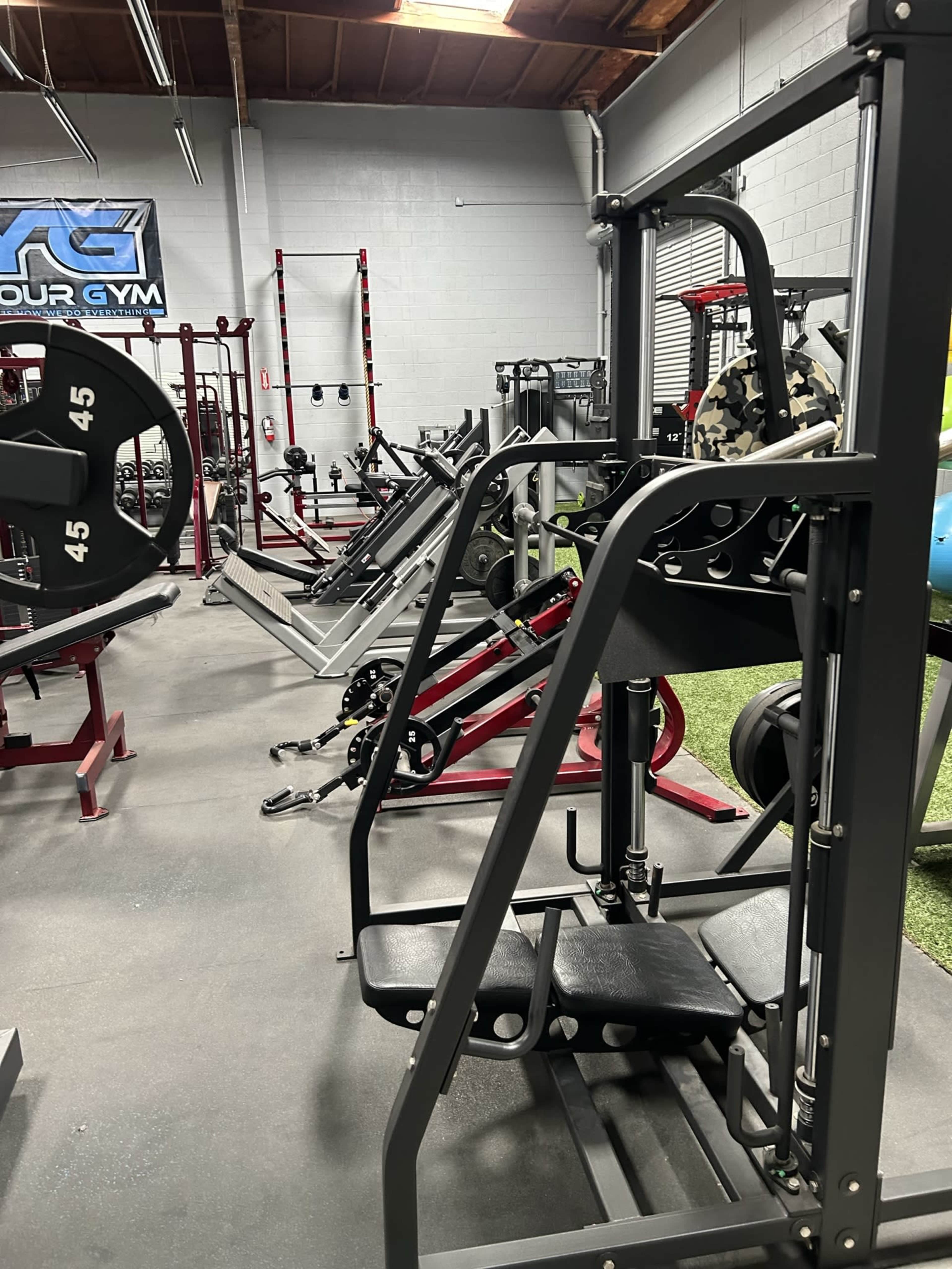 A gym interior with various weightlifting machines and equipment arranged neatly on the floor.