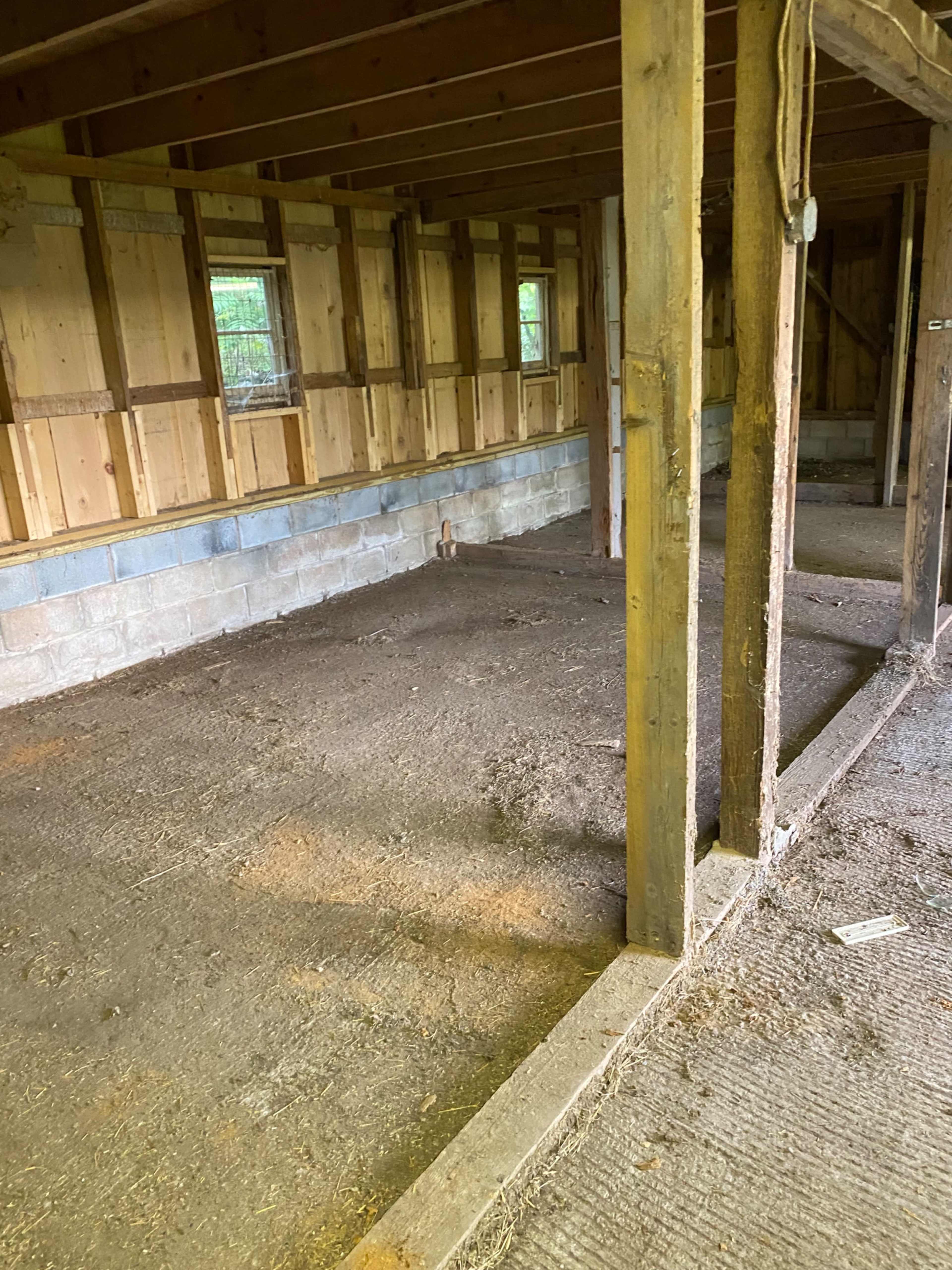 An empty barn interior with wooden beams and a dirt floor.