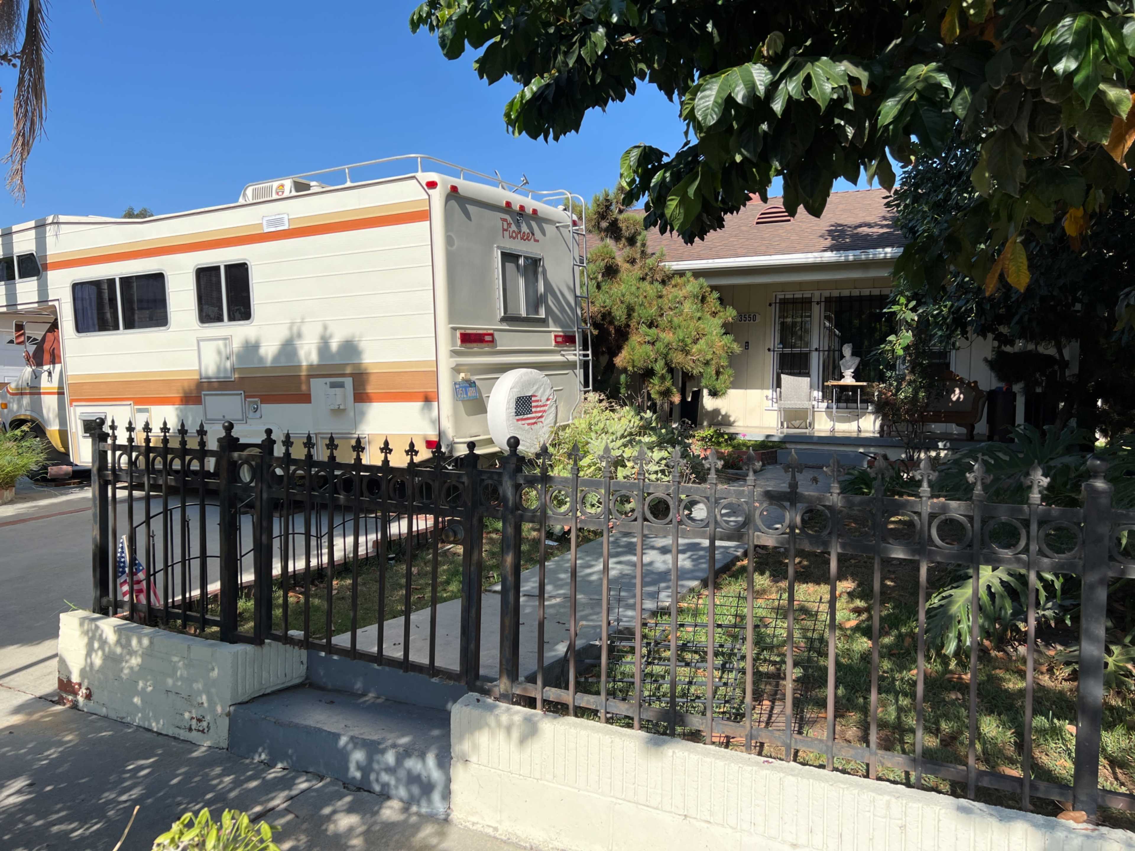 A recreational vehicle is parked in front of a house with a decorative fence and a well-kept yard.