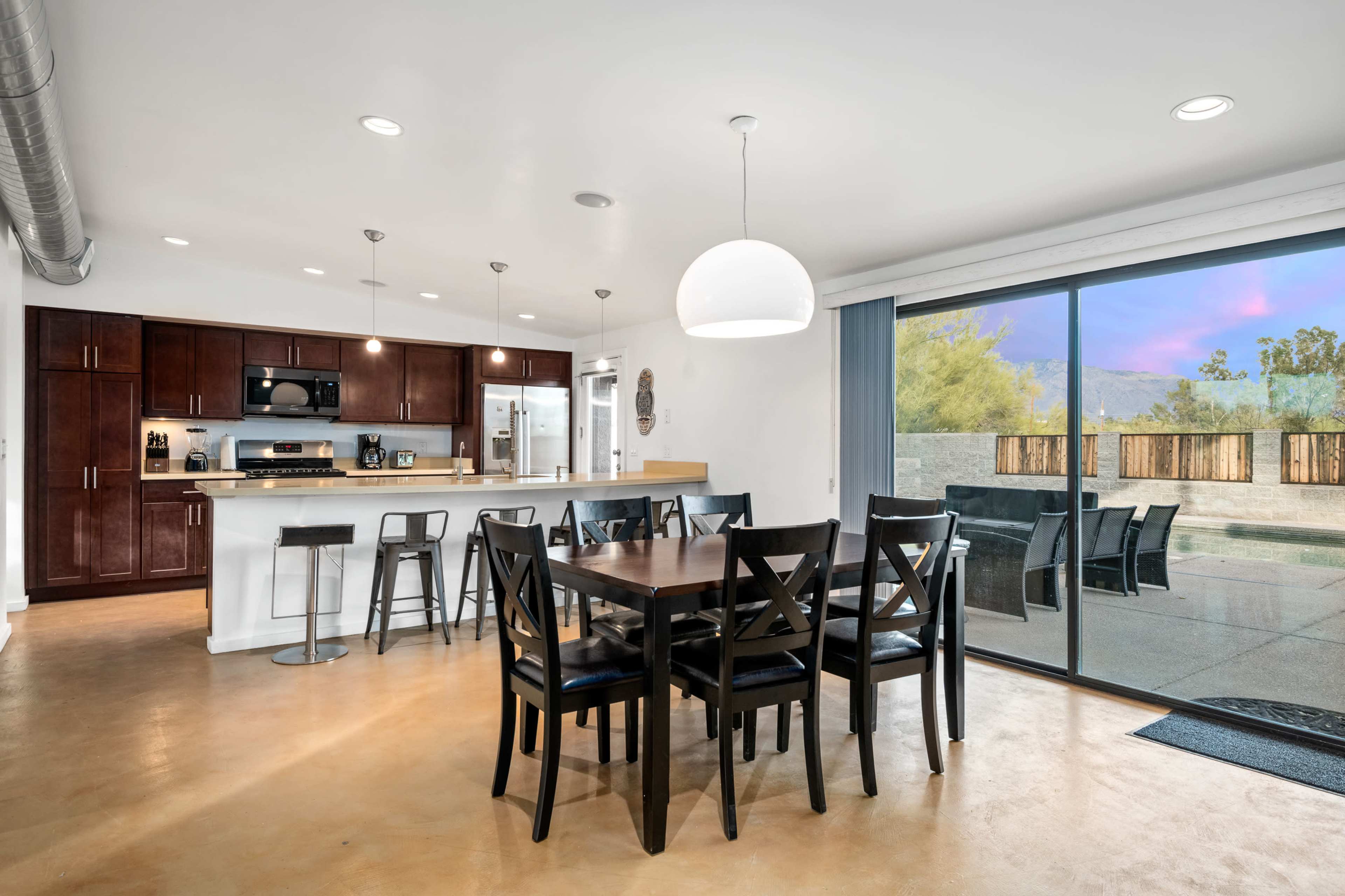 A modern kitchen and dining area features dark wooden cabinets, stainless steel appliances, and a glass sliding door opening to an outdoor patio.