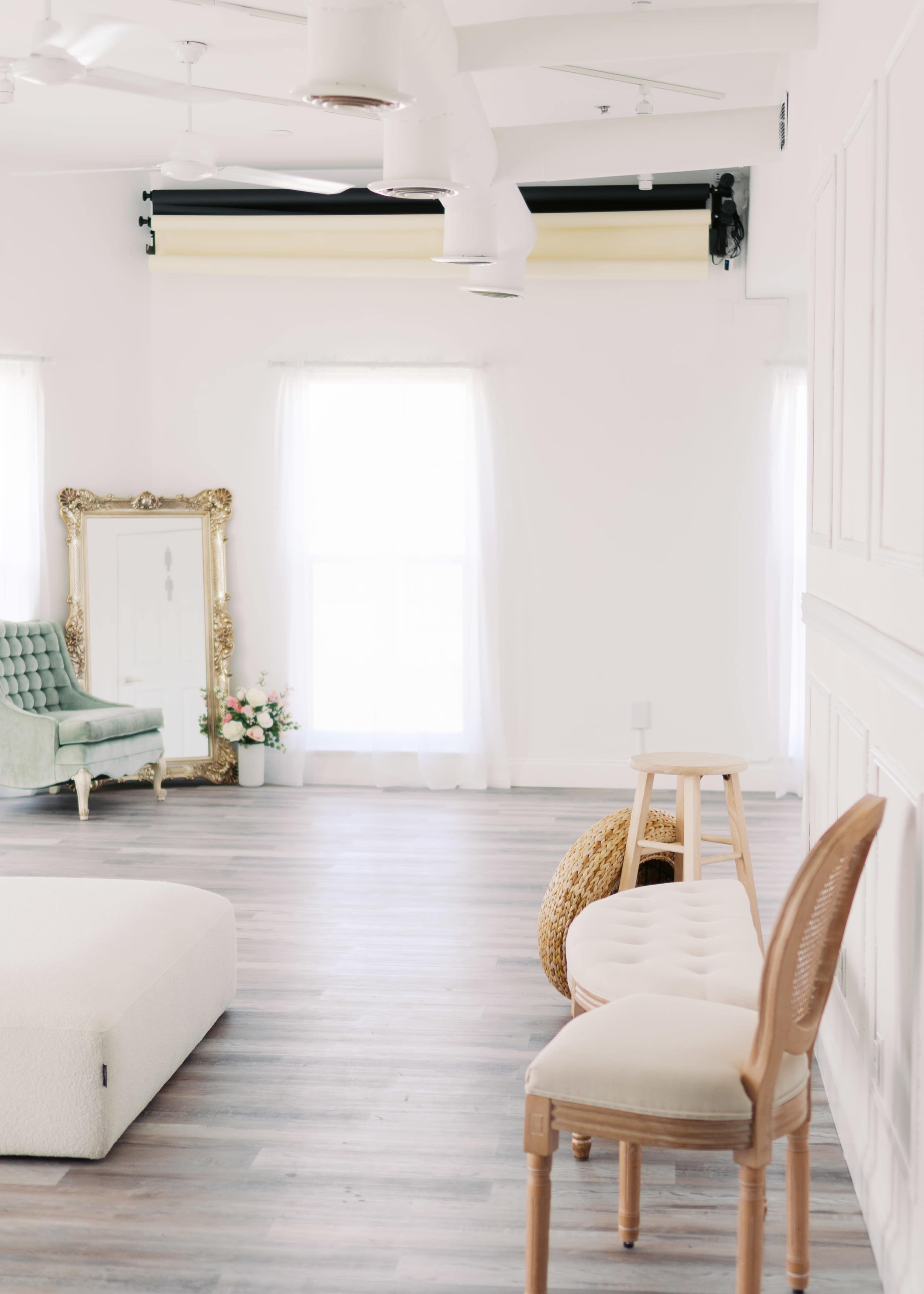 The image features a bright, airy room with light wood flooring, a green chair with ornate detailing, a large mirror, and minimal decorative elements.
