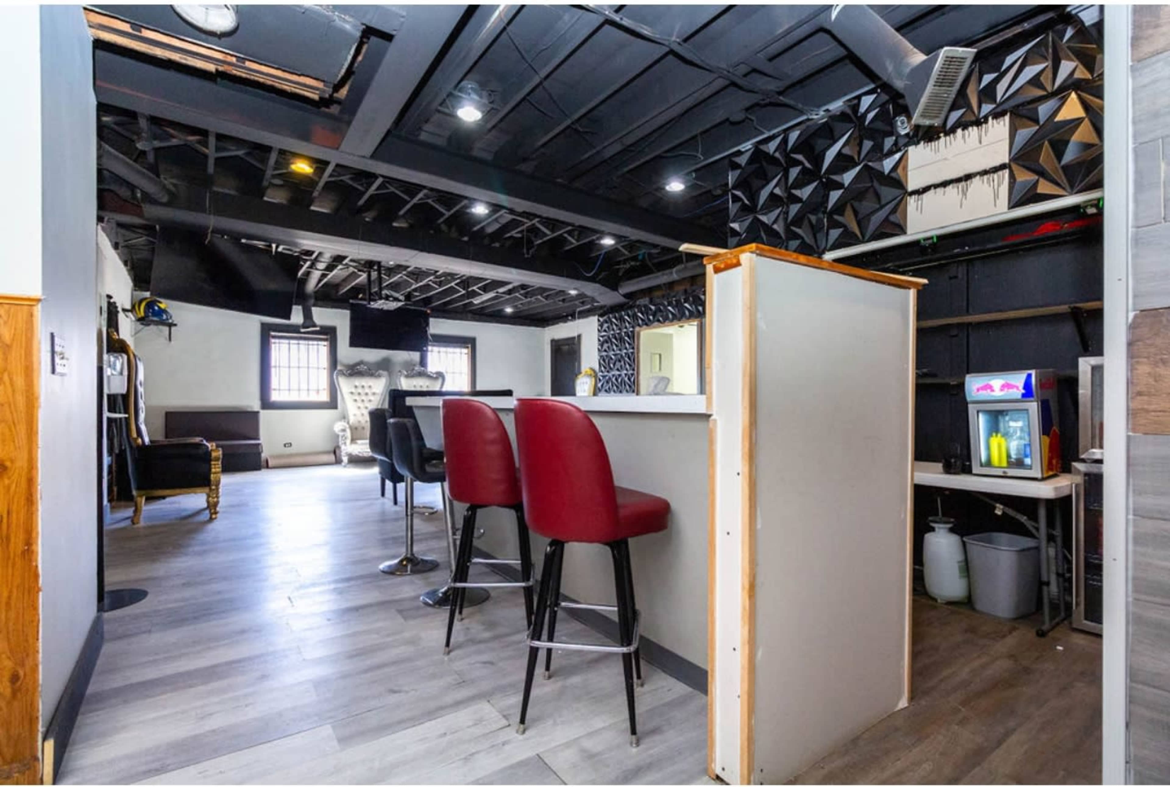 The image shows a modern interior space featuring a bar counter with red stools, a black ceiling, and geometric wall designs.