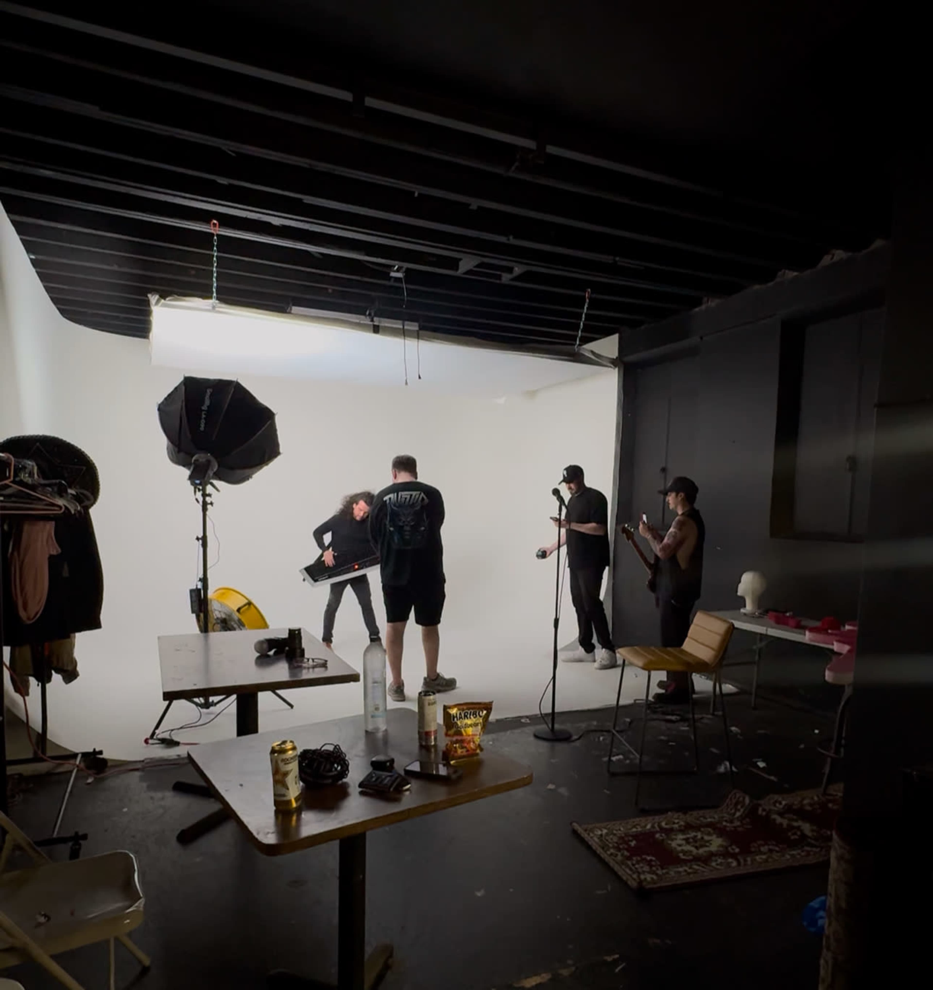 A group of four people is working in a photography studio, with one person posing in front of a bright white backdrop while others assist and set up equipment.
