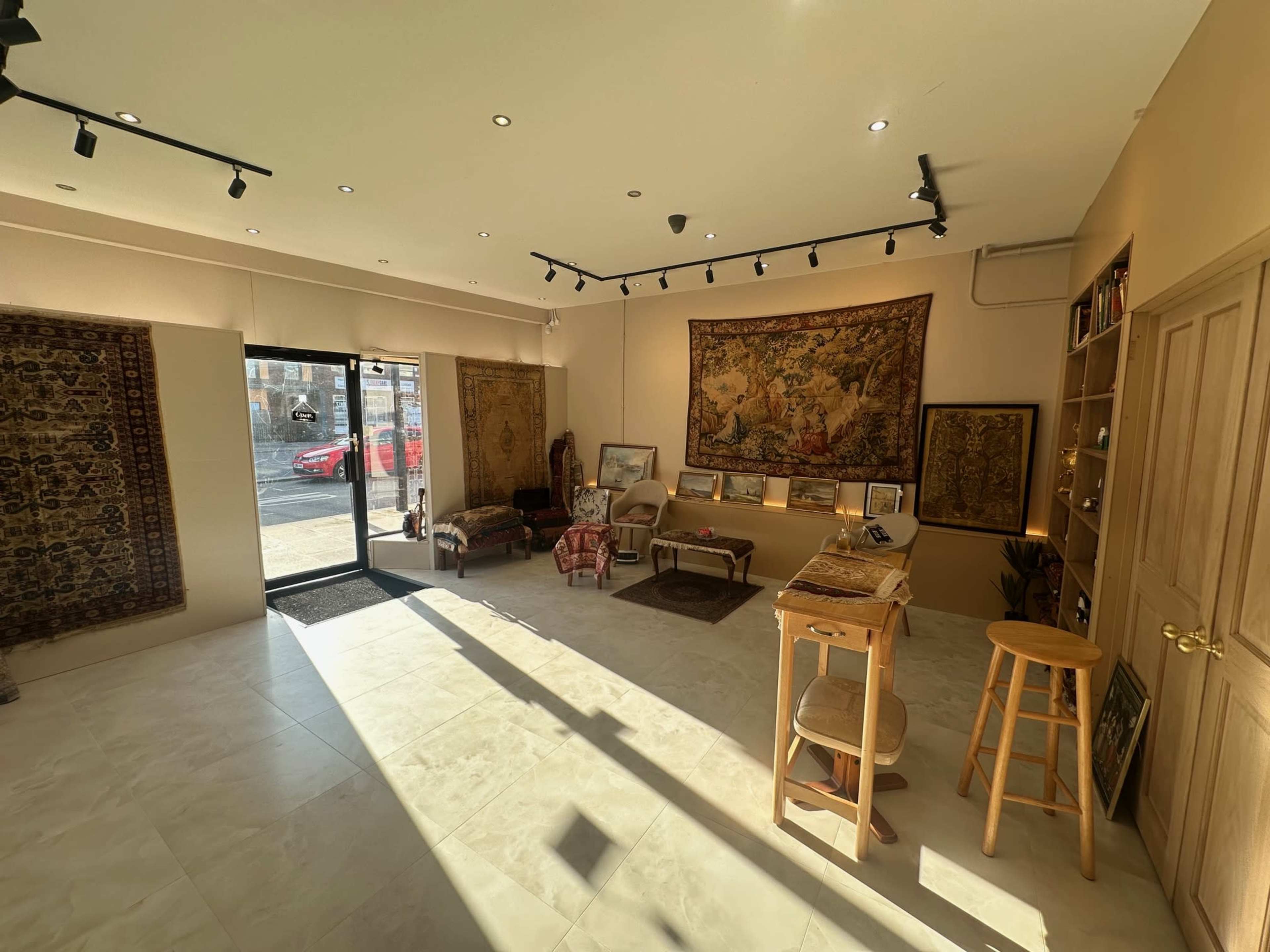 The image shows an interior of a gallery or shop featuring decorative rugs and a large world map on the wall, with a wooden counter and stools placed in the center.