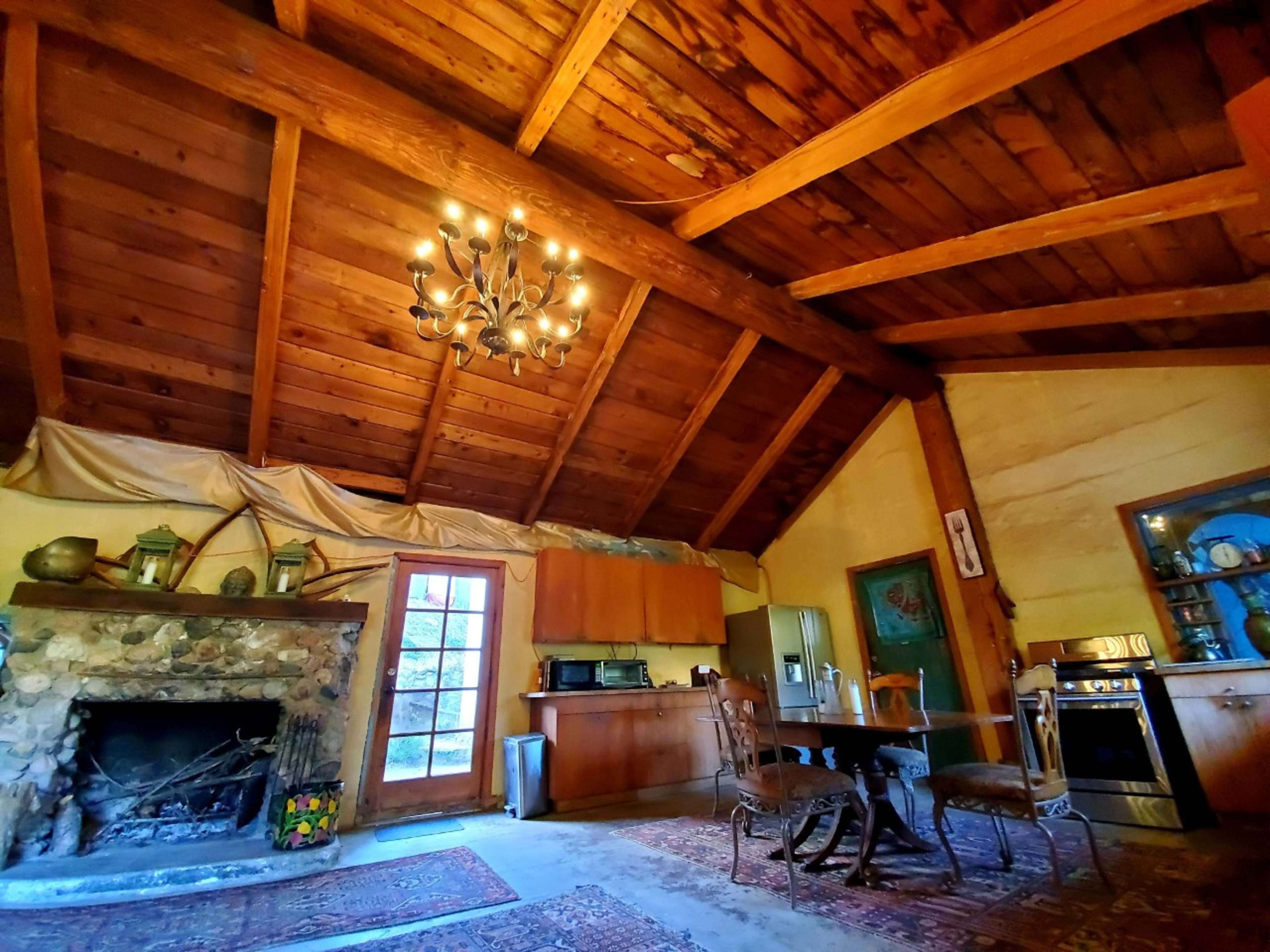 The interior of a rustic cabin features wooden beams, a stone fireplace, and a dining table with two chairs.