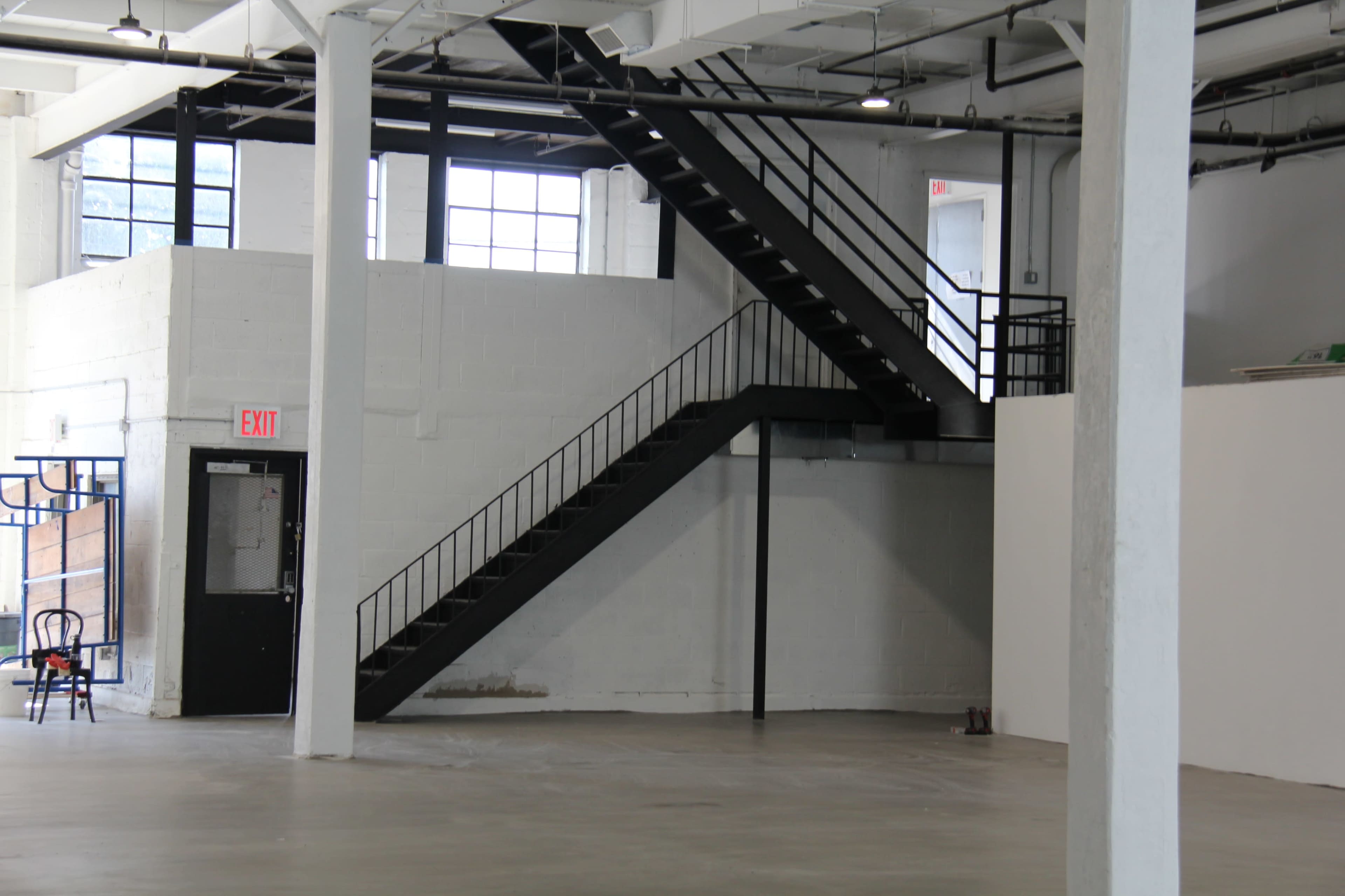 A spacious, industrial-style interior featuring a black metal staircase leading to an upper level, with large windows illuminating the area.