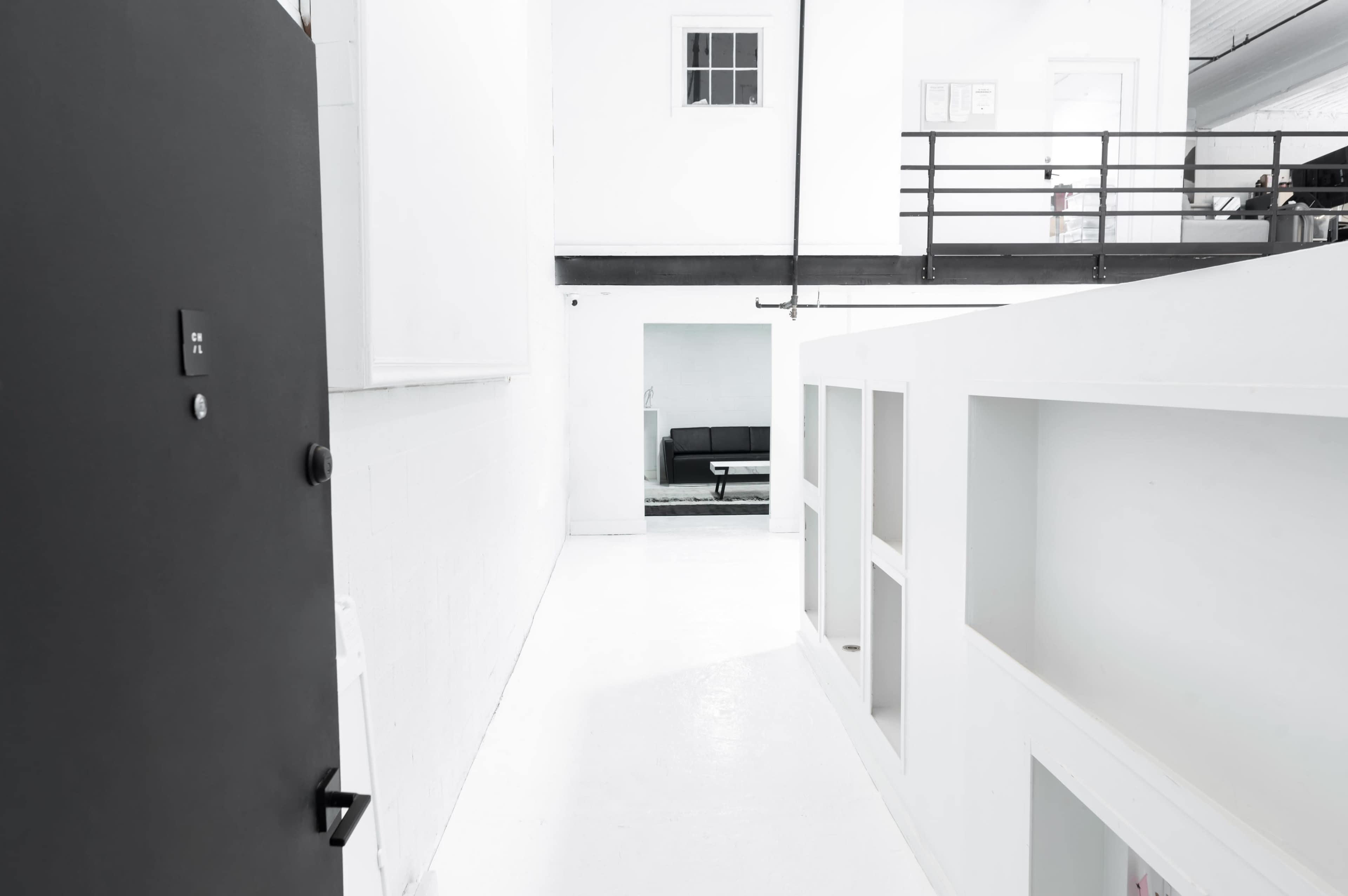 A stark, white interior hallway leading to a seating area visible through an open doorway.