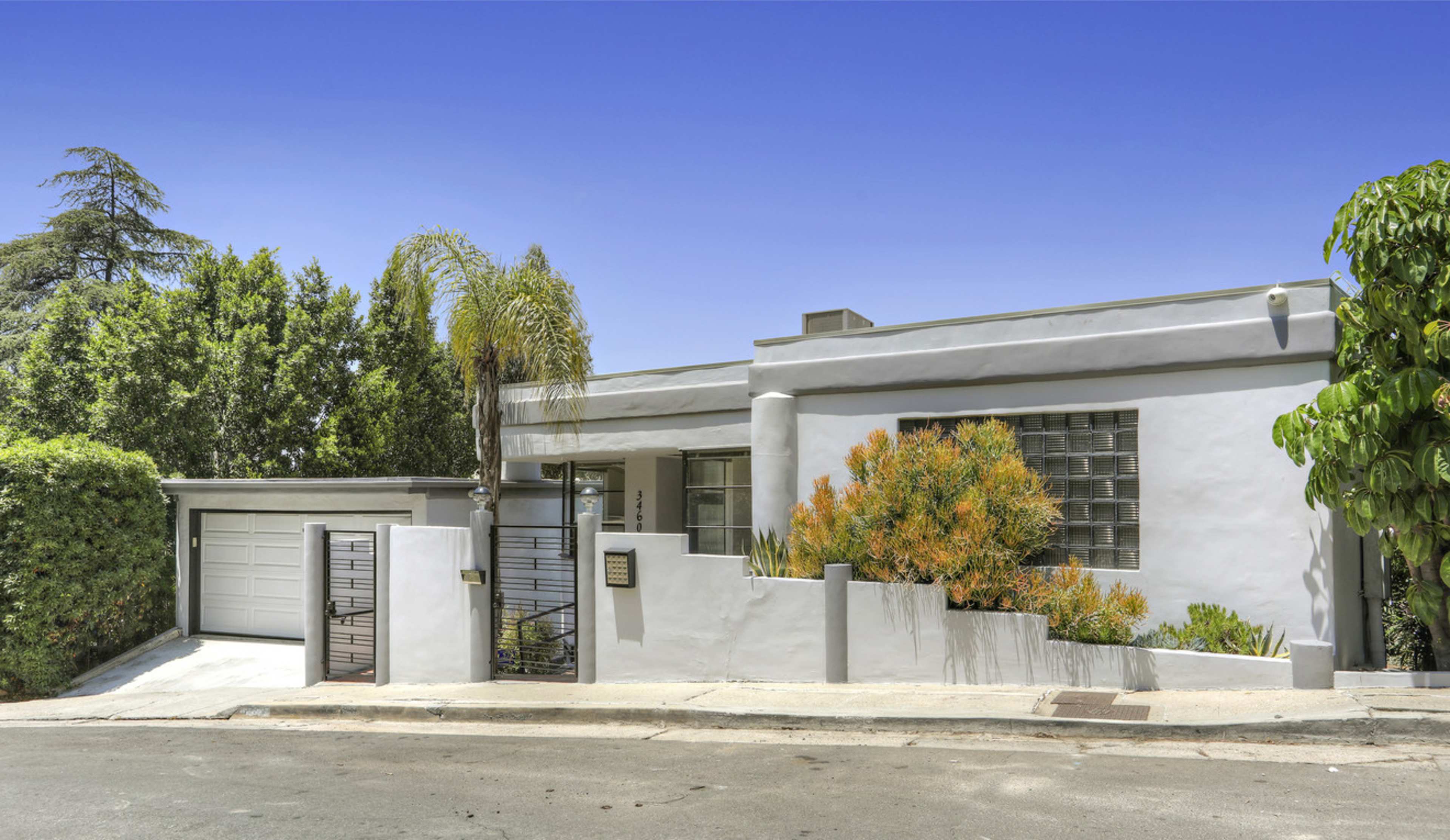 The image shows a modern, single-story house with a landscaped front yard and a garage on the side.