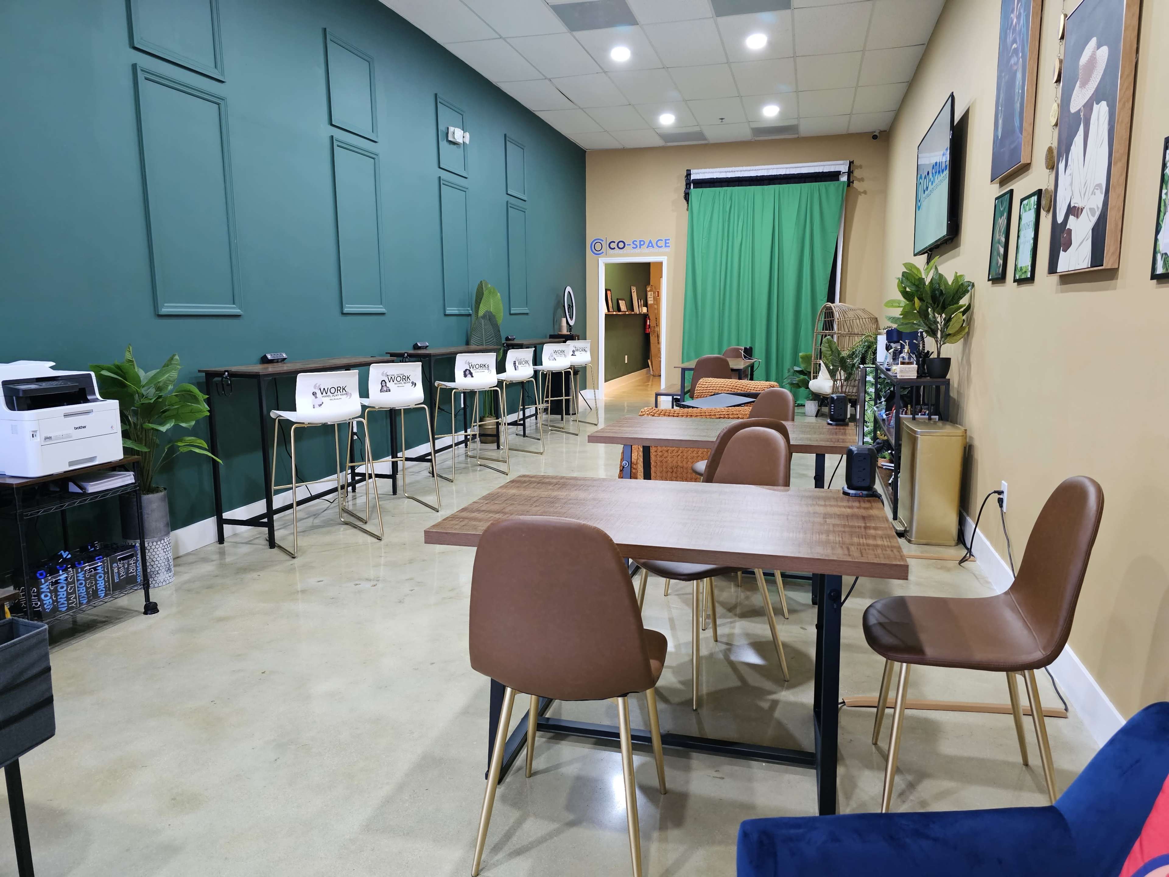 A modern workspace with green accent walls, a row of bar stools, and tables set up for collaboration.