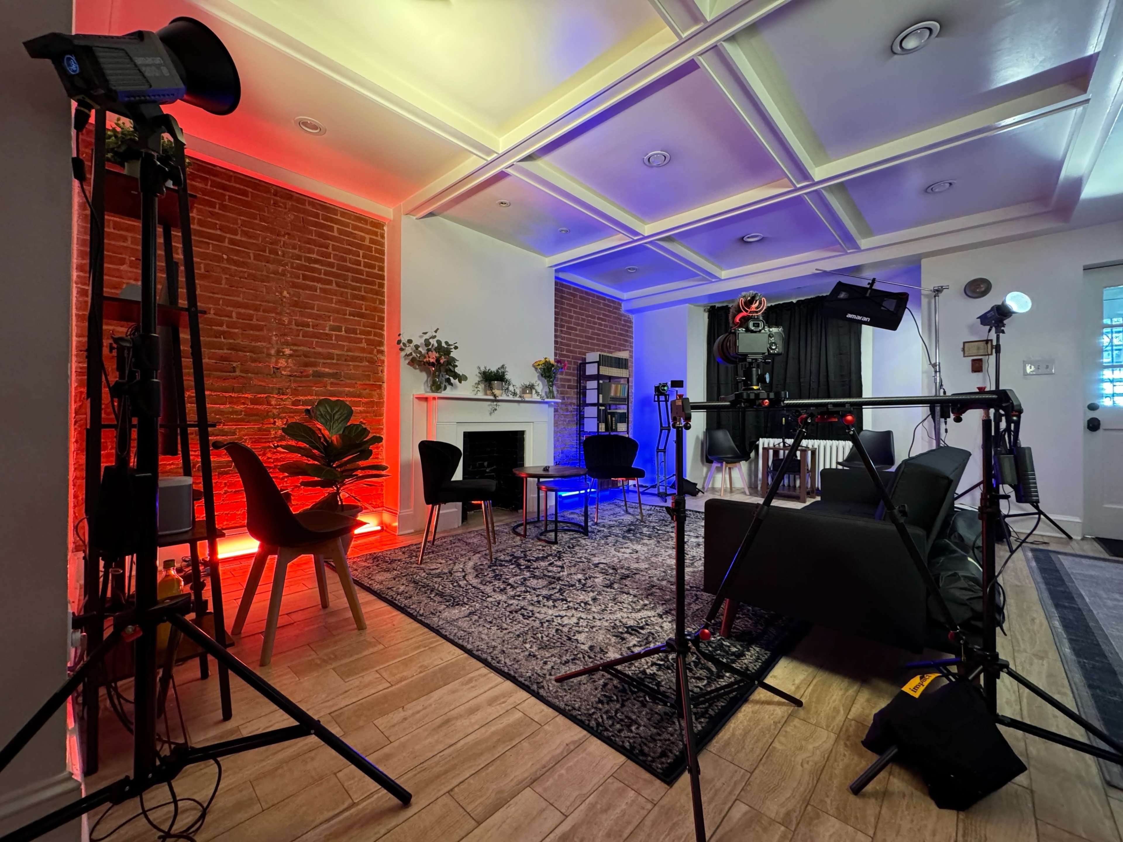 A modern studio setup featuring a seating area, lighting equipment, and a backdrop against a brick wall.