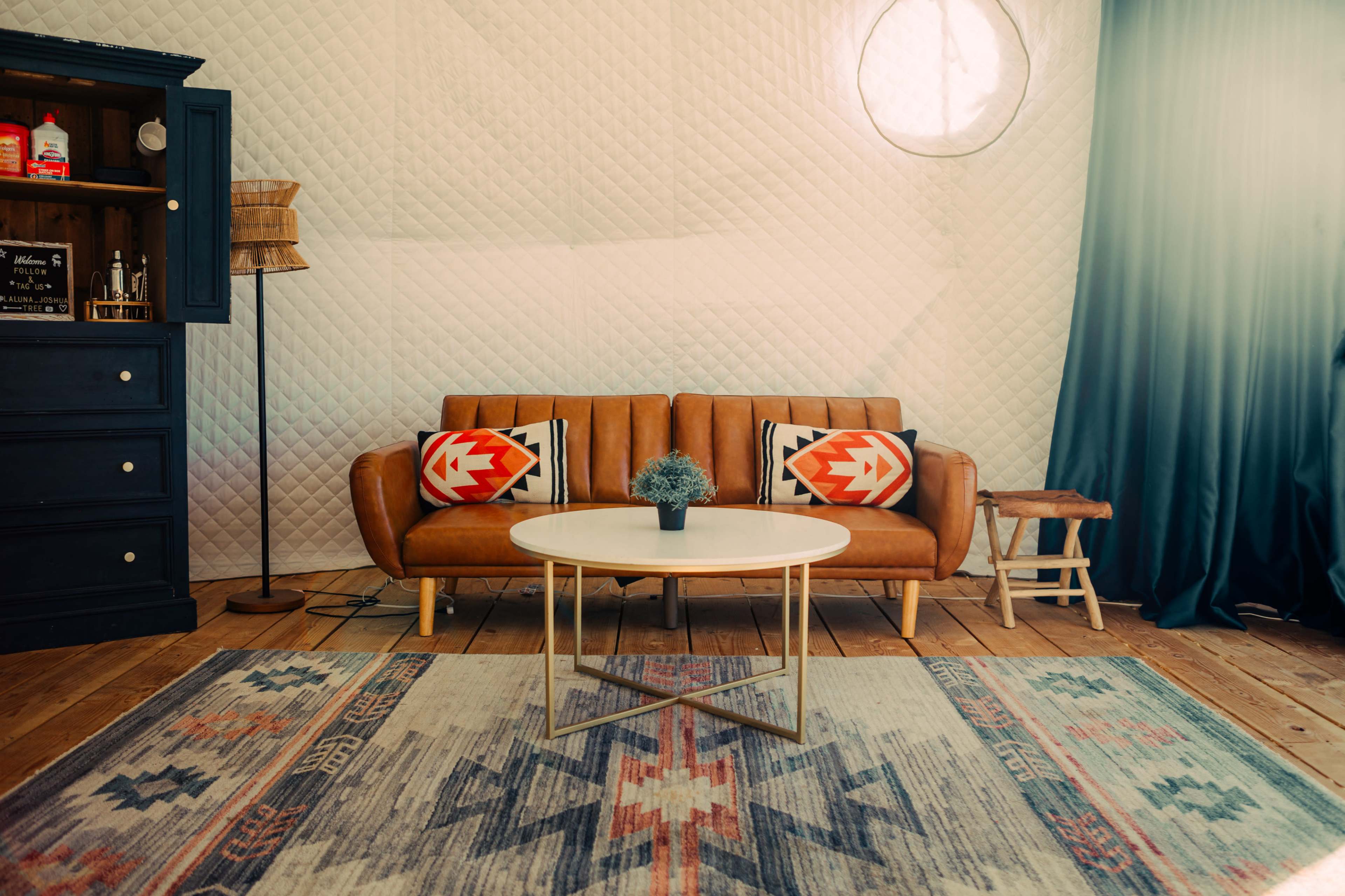 The image features a stylish living room with a brown leather sofa, a round coffee table, and a blue curtain, all set against a textured white wall.