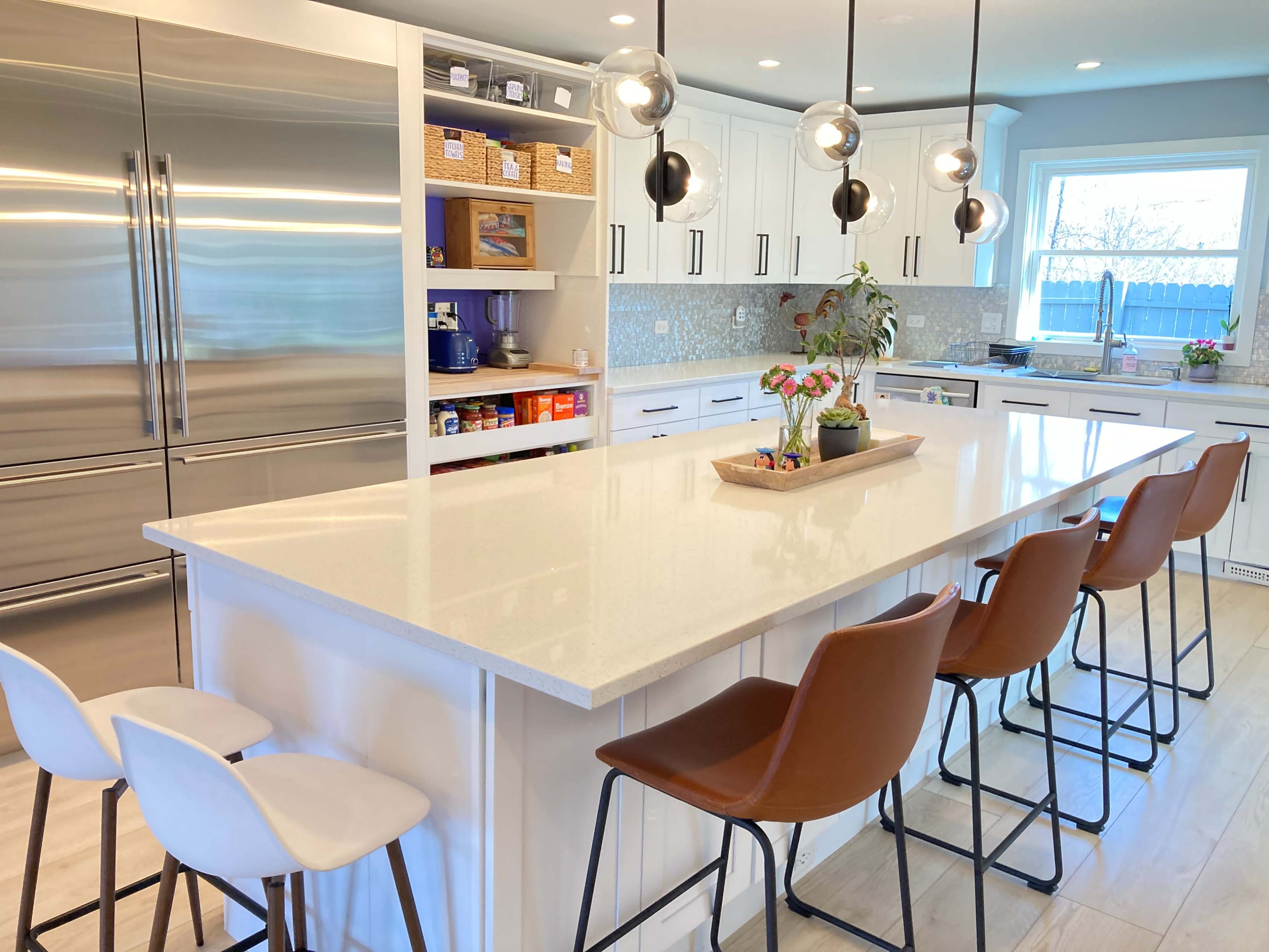 A modern kitchen featuring a large island with bar stools, stainless steel appliances, and white cabinetry.