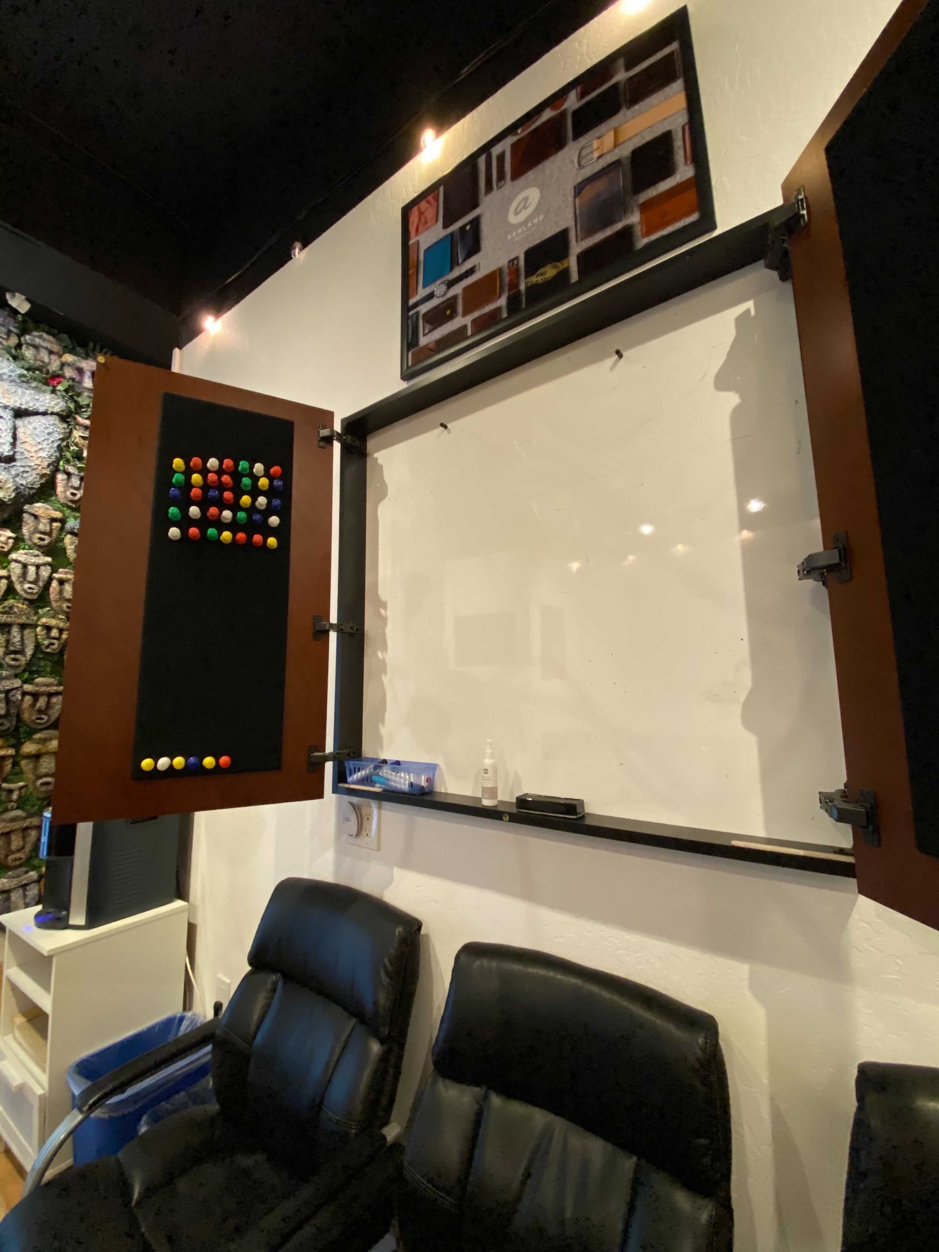 A wall-mounted whiteboard with two side panels containing colorful magnets, flanked by two black chairs.