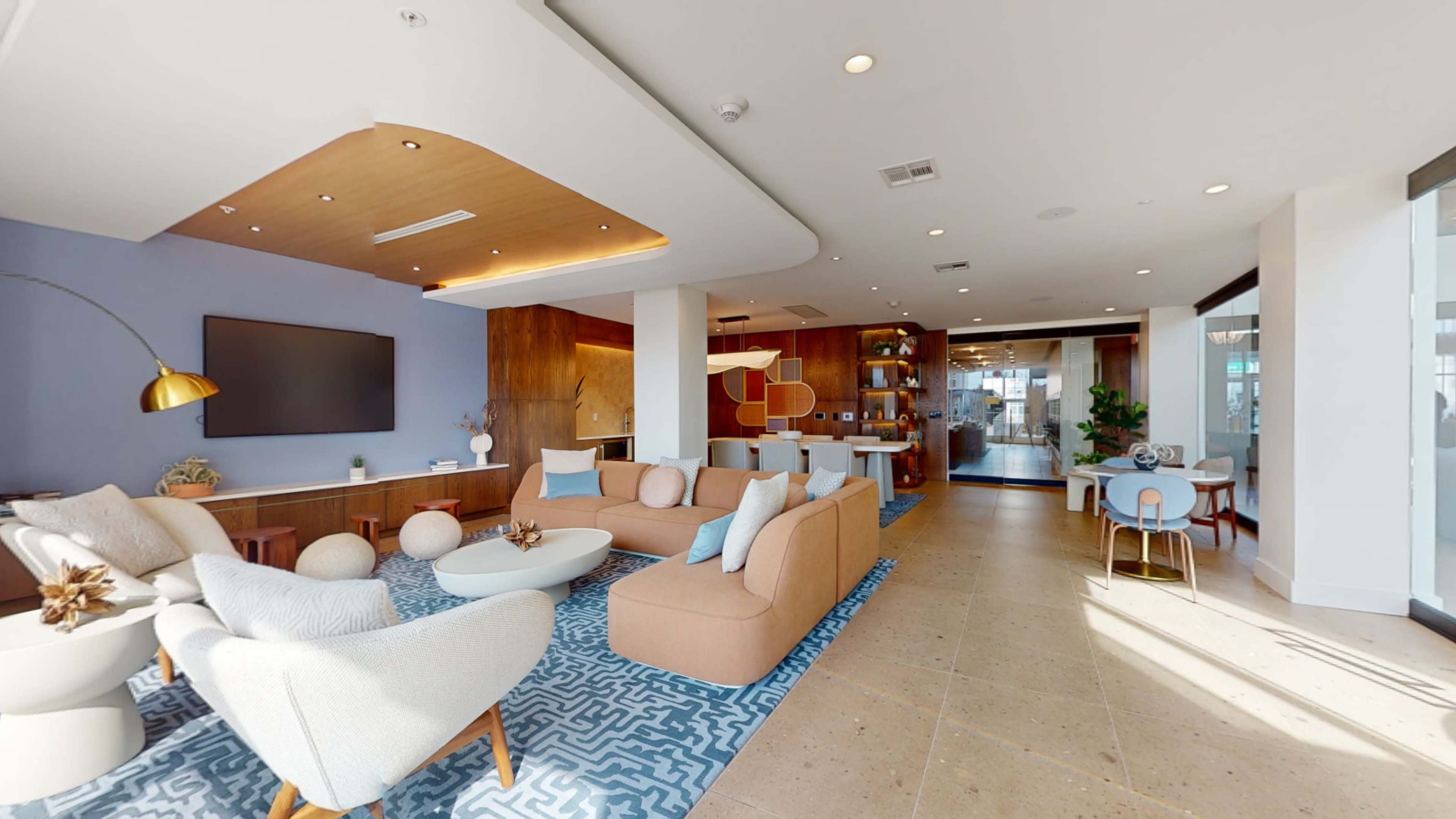 The image shows a modern lobby area with seating arrangements, a television on the wall, and a reception desk nearby.