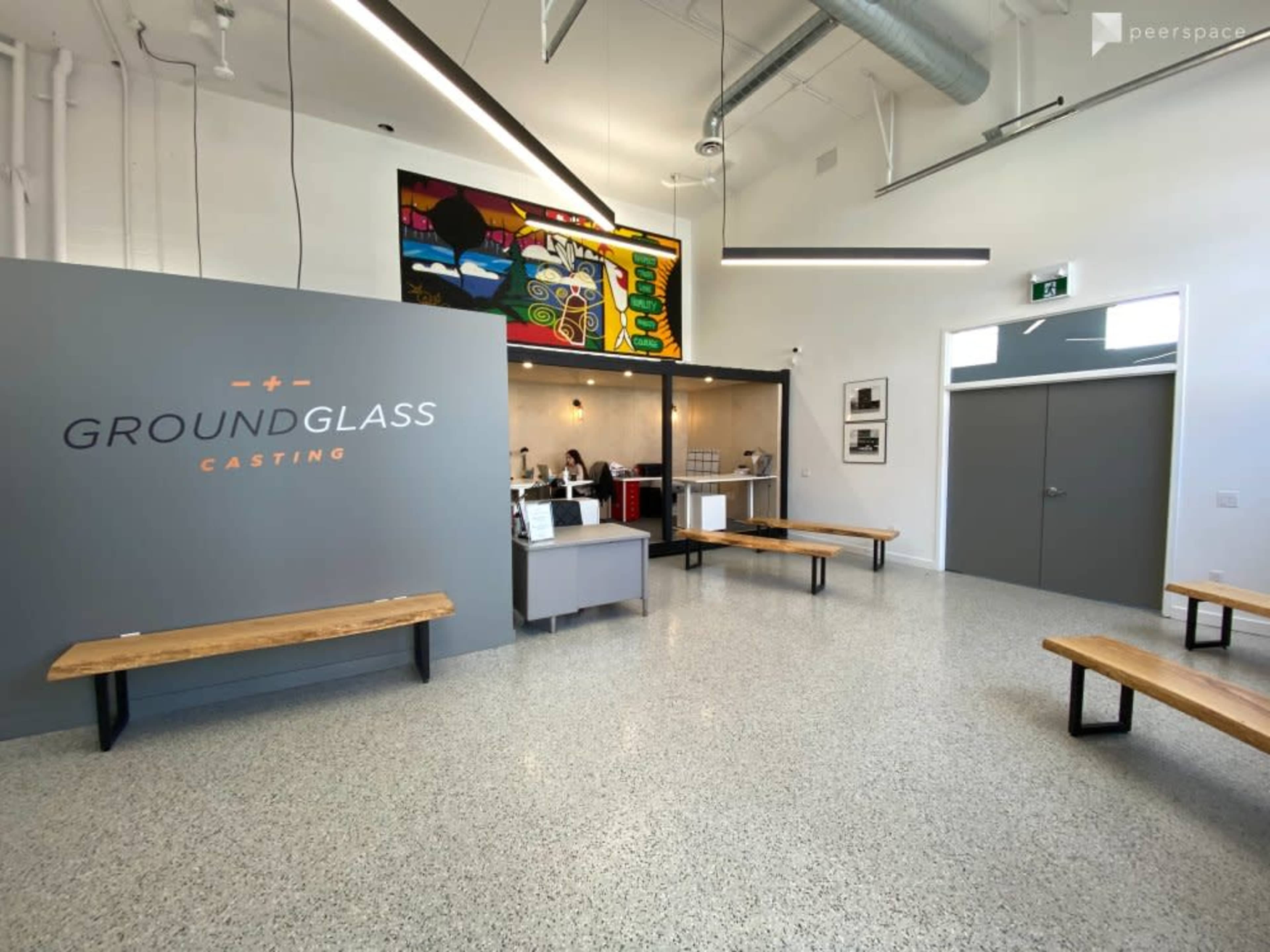 An interior casting office with a reception area, featuring a logo on the wall, wooden benches, and colorful artwork.