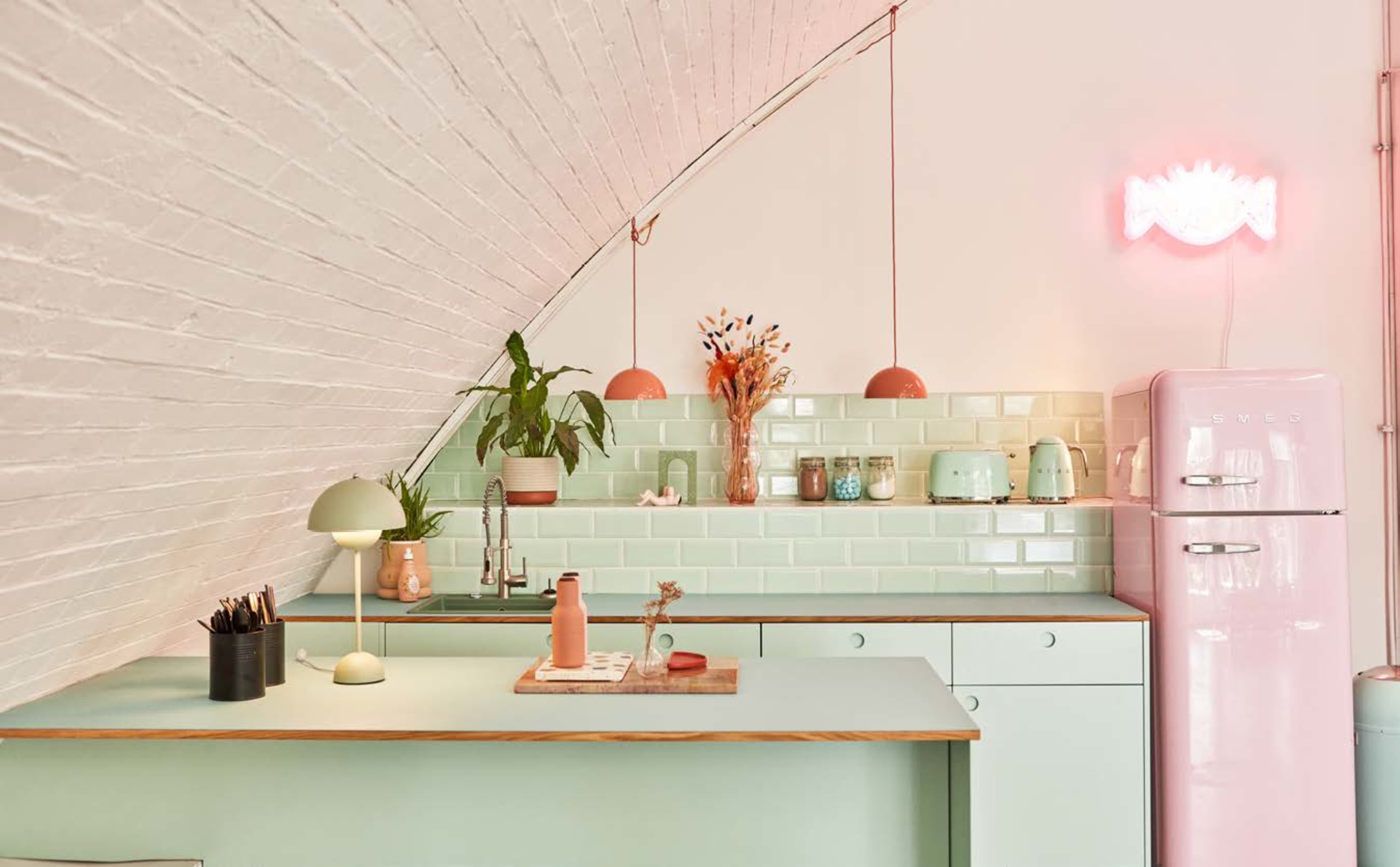 A modern kitchen featuring pastel green cabinets, a pink refrigerator, and decorative items on the counter and shelves.