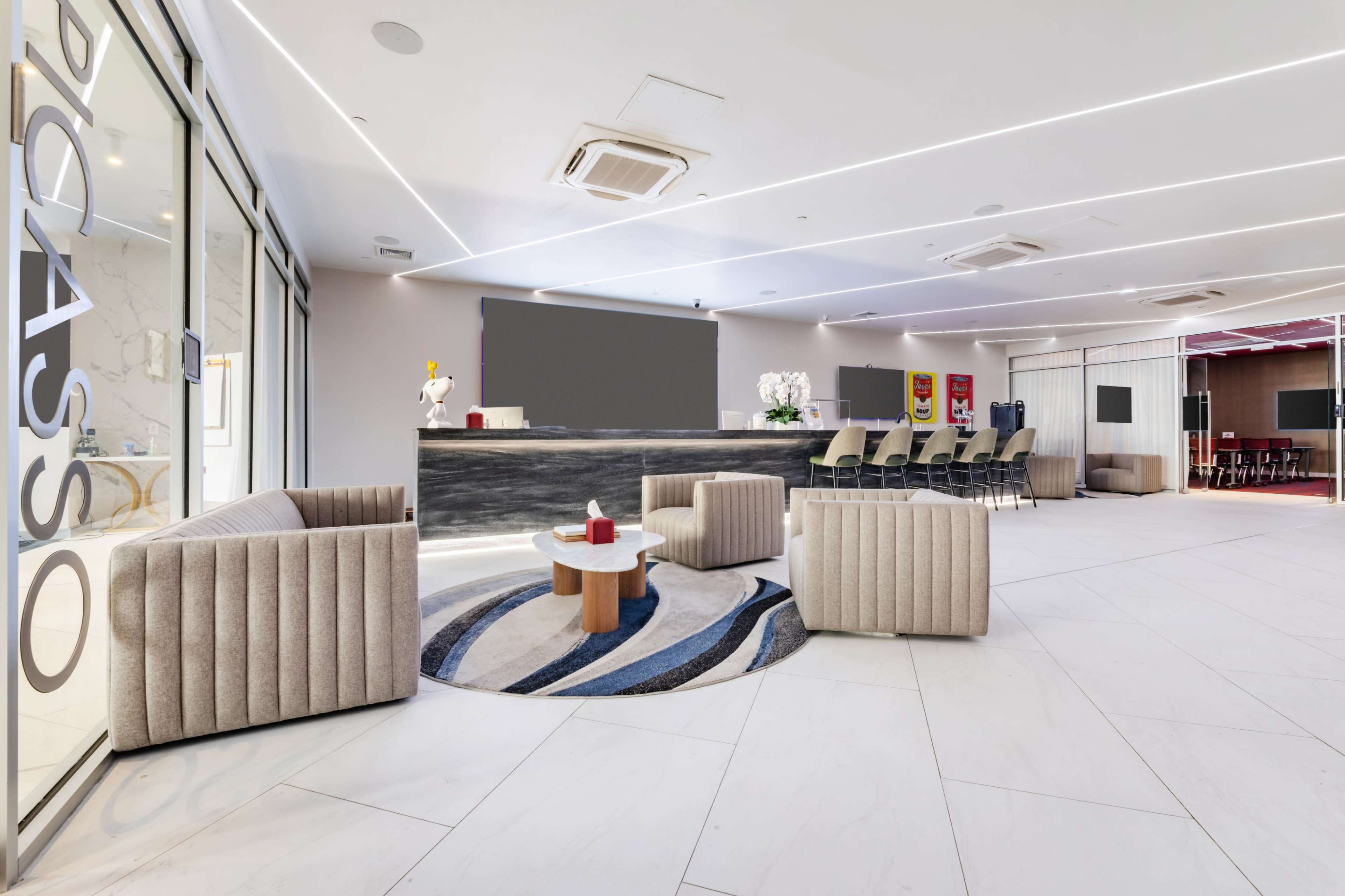 The image shows a modern lobby area with contemporary furniture, including plush seating and a reception desk, accented by stylish decor and a patterned area rug.