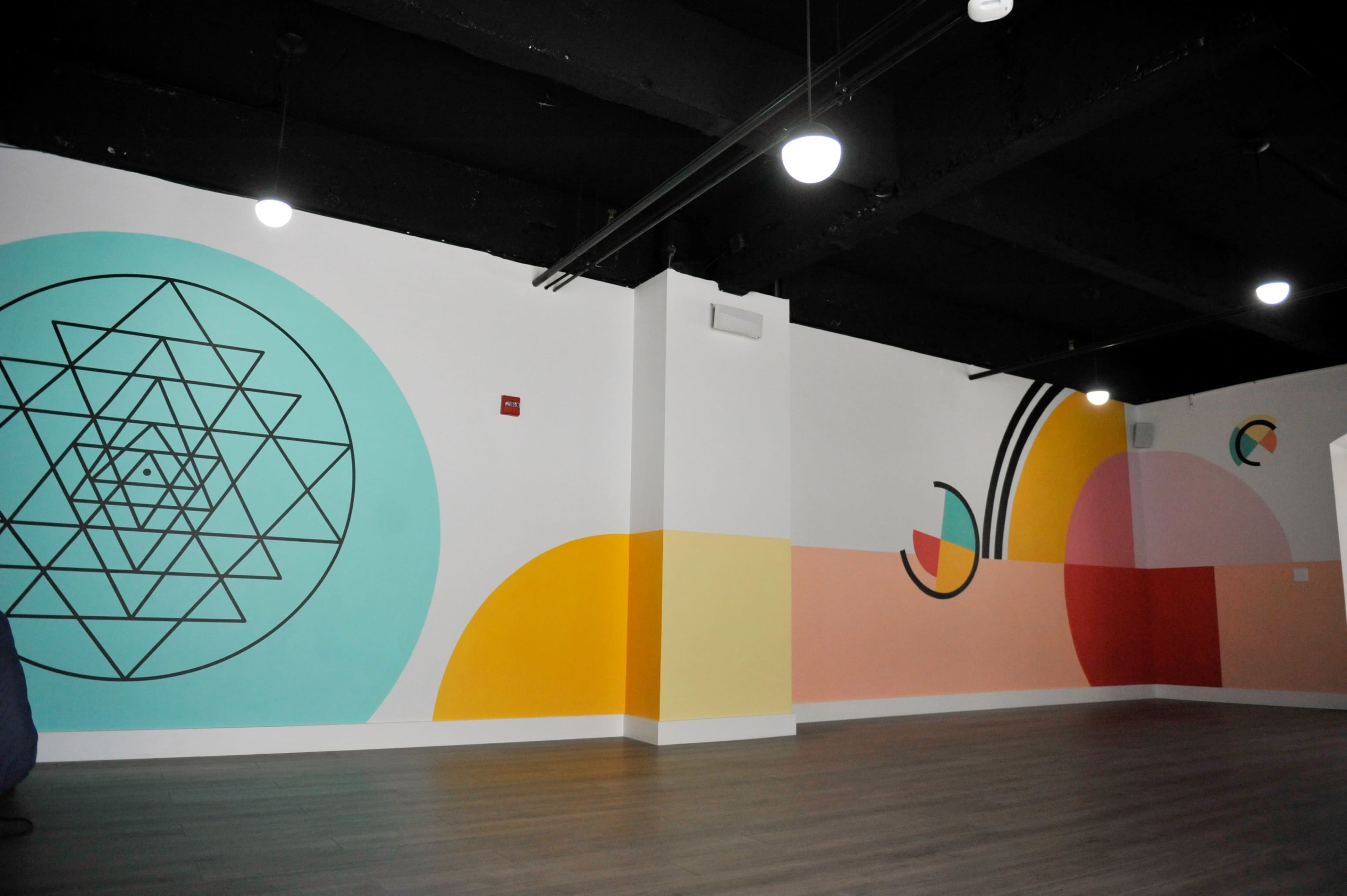 A spacious room with a hardwood floor and walls featuring colorful geometric mural designs in various shapes.