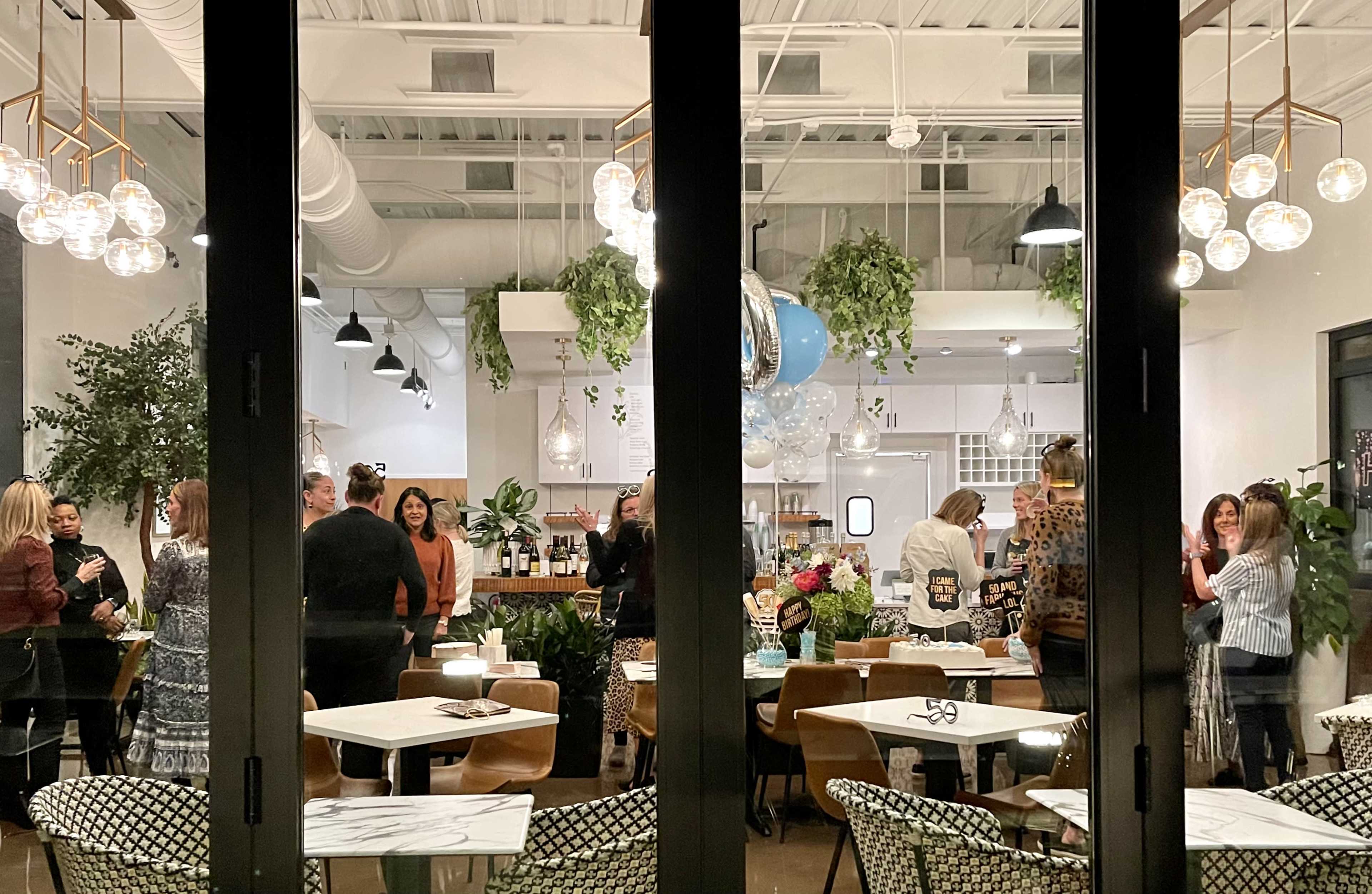 A group of people socializes inside a modern café adorned with plants and stylish lighting fixtures.