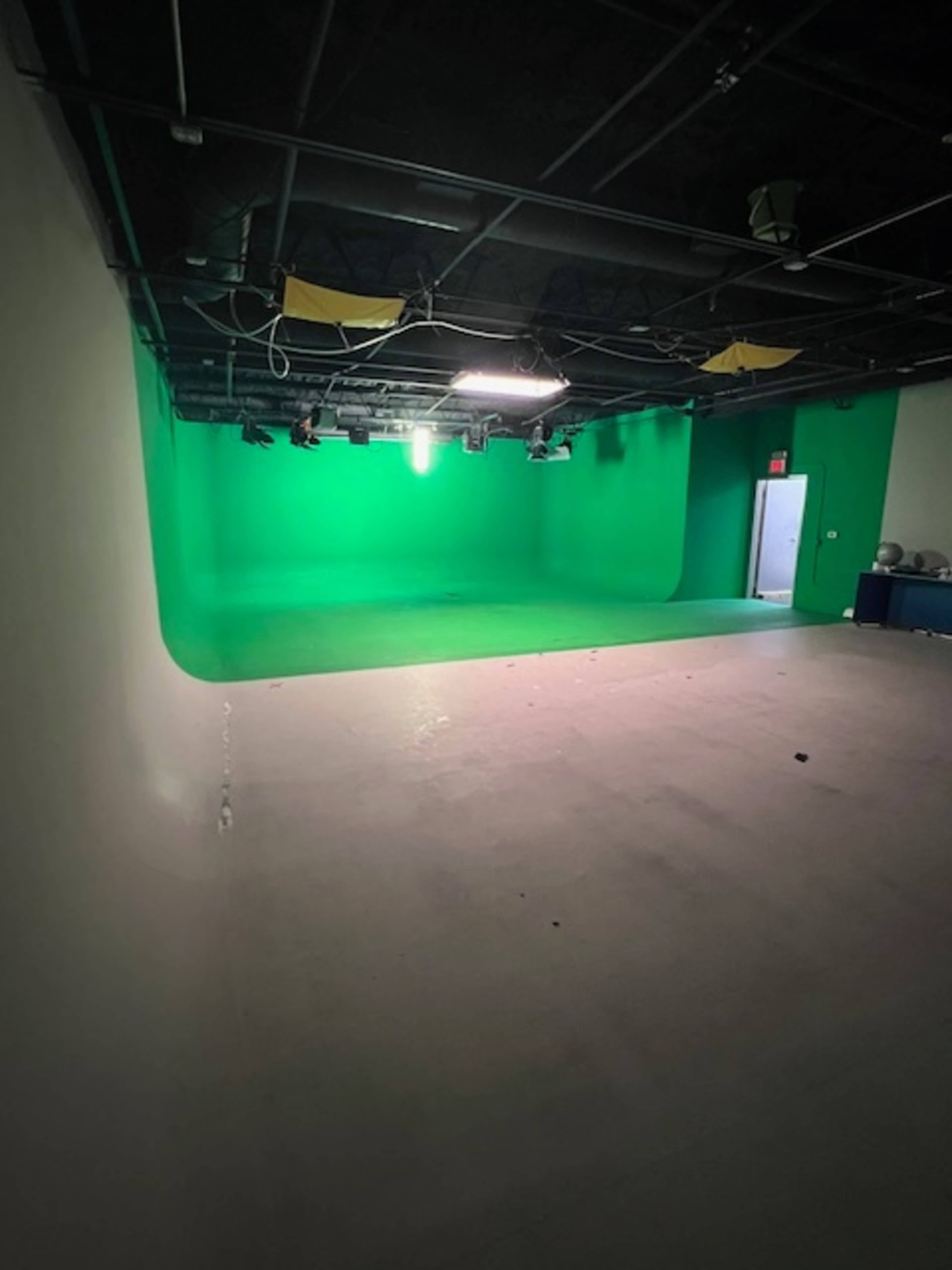 A spacious green screen studio with a well-lit backdrop and an adjacent door.