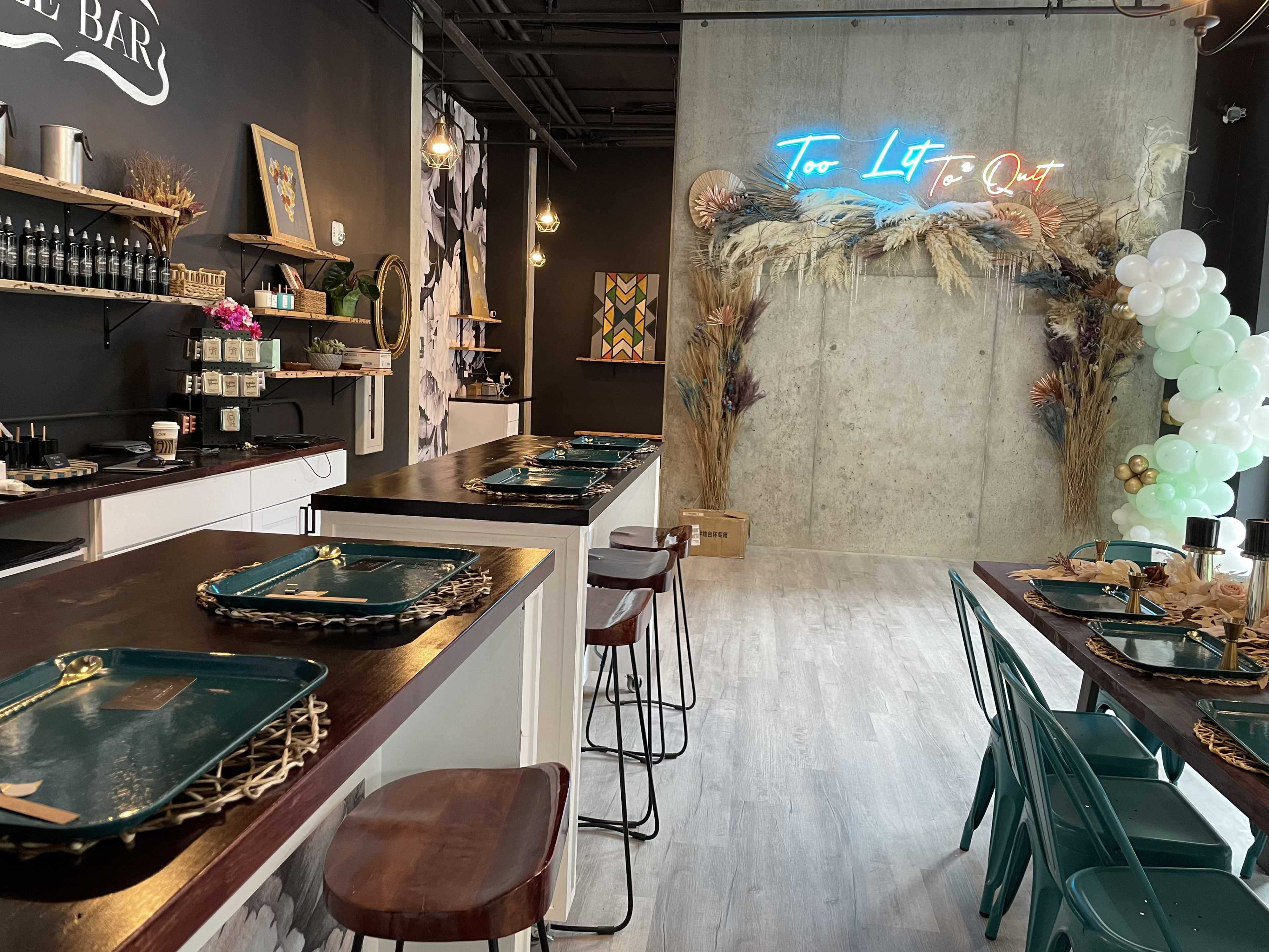 A modern café interior with wooden tables, teal chairs, and a neon sign against a concrete wall.