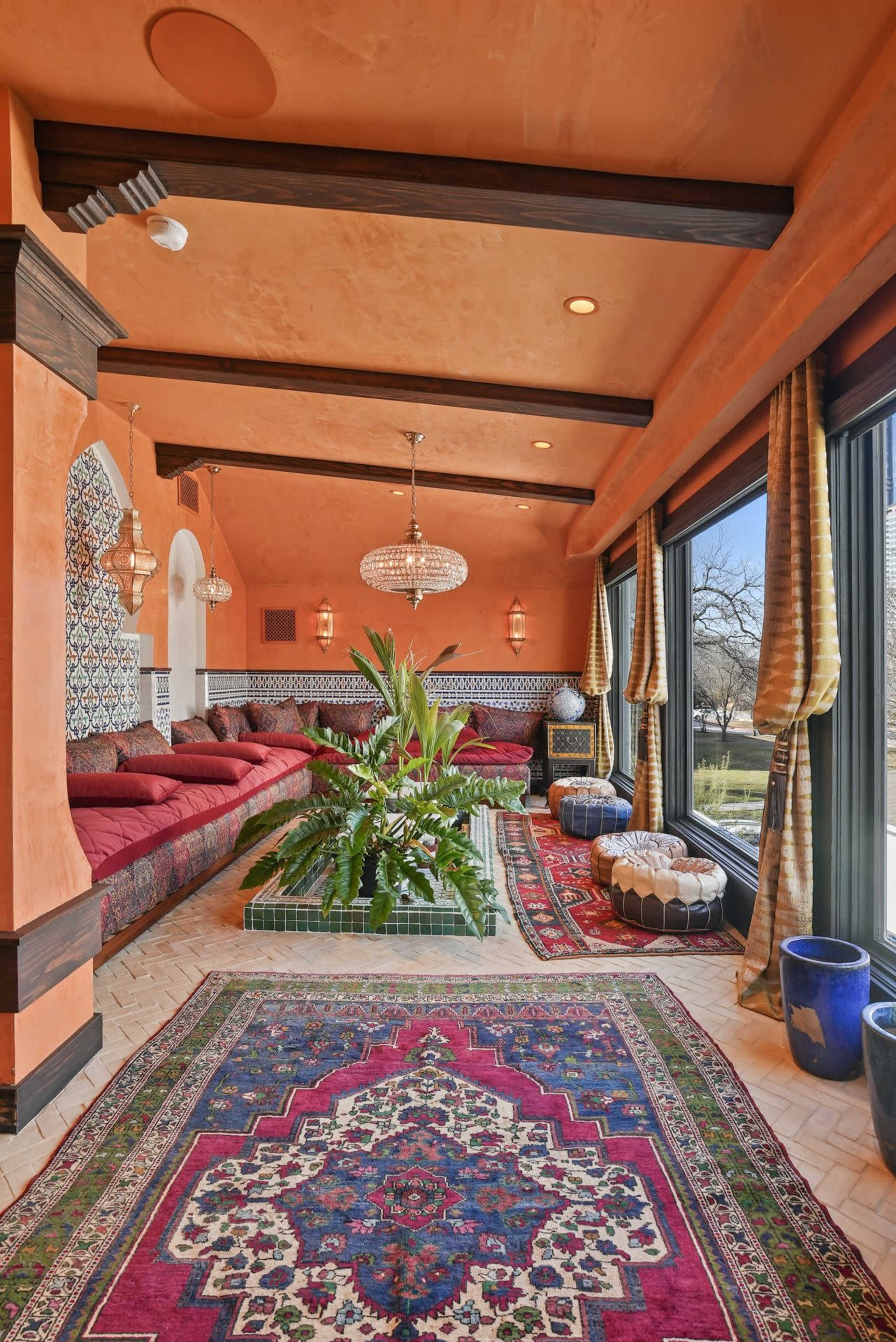 The image shows a vibrant, Moroccan-inspired indoor space with colorful cushions, patterned tiles, and decorative plants.
